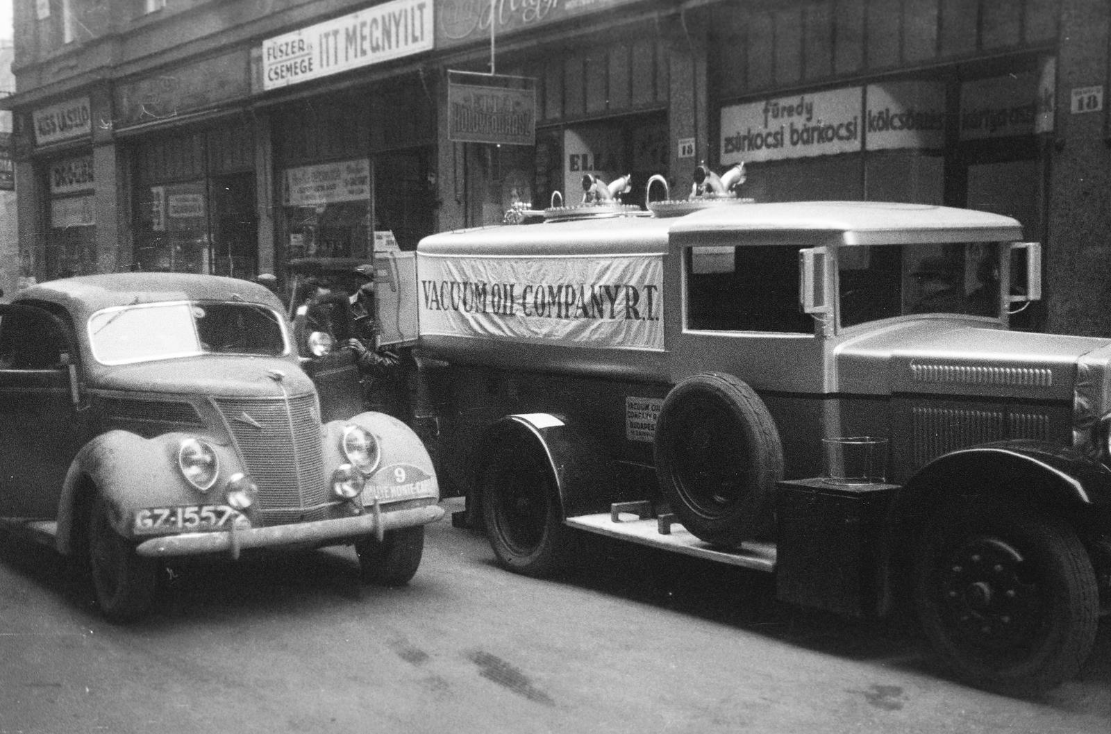 Magyarország, Budapest V., Irányi utca, a 18-as számú ház előtt a Vacuum Oil Company Rt. tartályautója. Az ekkor csillagtúraként megrendezett Monte-Carlo Rallye Athénből induló 9-es rajtszámú, későbbi győztes holland Bakker-Schut Gerard - Ton Karel versenyzőpáros, Ford V8 típusú gépjárműve., 1938, Inkey Tibor, automobil, Ford-márka, angol felirat, Mobiloil-márka, Ford V8, tankautó, rendszám, gépkölcsönző, vegyesbolt, Budapest, Fortepan #306018