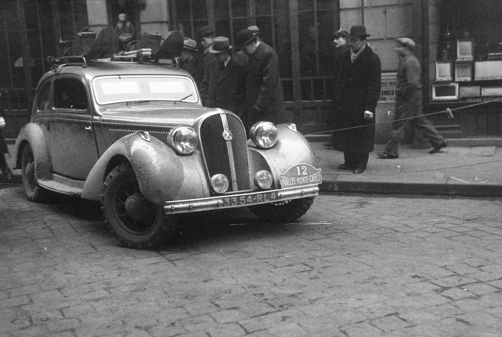 Magyarország, Budapest V., Curia utca 1., a Veres Pálné utca sarkán álló ház előtt, az ekkor csillagtúraként megrendezett Monte-Carlo Rallye Athénból iduló 12-es rajtszámú, francia Trévoux Jean - Lesurque Marcel versenyzőpáros, Hotckiss típusú gépjárműve., 1938, Inkey Tibor, bámészkodás, automobil, Hotchkiss-márka, rendszám, rajtszám, tetőcsomagtartó, Budapest, Fortepan #306025