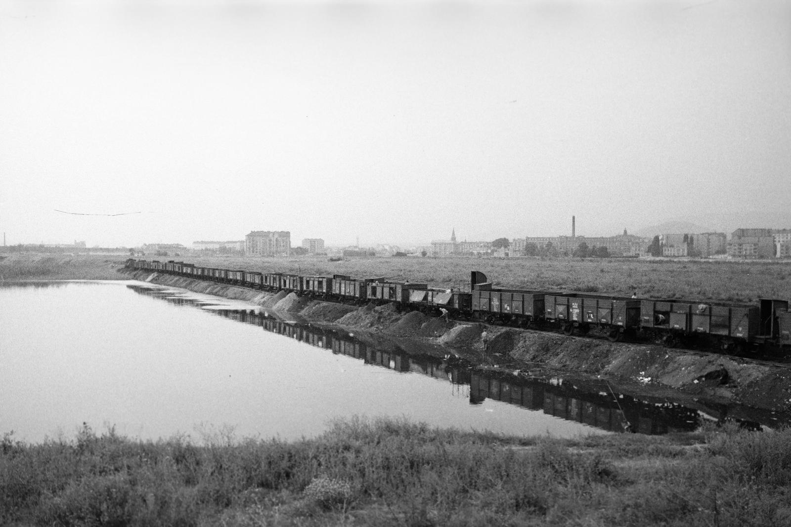 Magyarország, Budapest XI., a Lágymányosi-tó feltöltése. Háttérben balra egymagában a Budafoki út 81. saroképülete, középen a Magyar Advent templomának tornya, míg jobbra a Lágymányosi Dohánygyár (Budafoki út) kéménye és épületei látszódnak, ettől jobbra a távolban a Sas-hegy., 1937, Inkey Tibor, vízpart, vasúti szerelvény, Budapest, Fortepan #306142