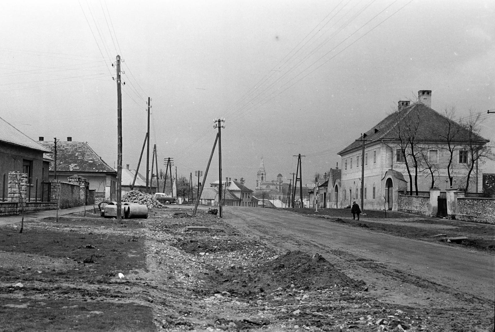 Magyarország, Zirc, Kossuth Lajos utca, jobbra az 1723-ban épült barokk fogadó, a távolban a Ciszterci Apátság épületegyüttese látható., 1960, Gazda Anikó, földút, villanypózna, távíróoszlop, Fortepan #307747