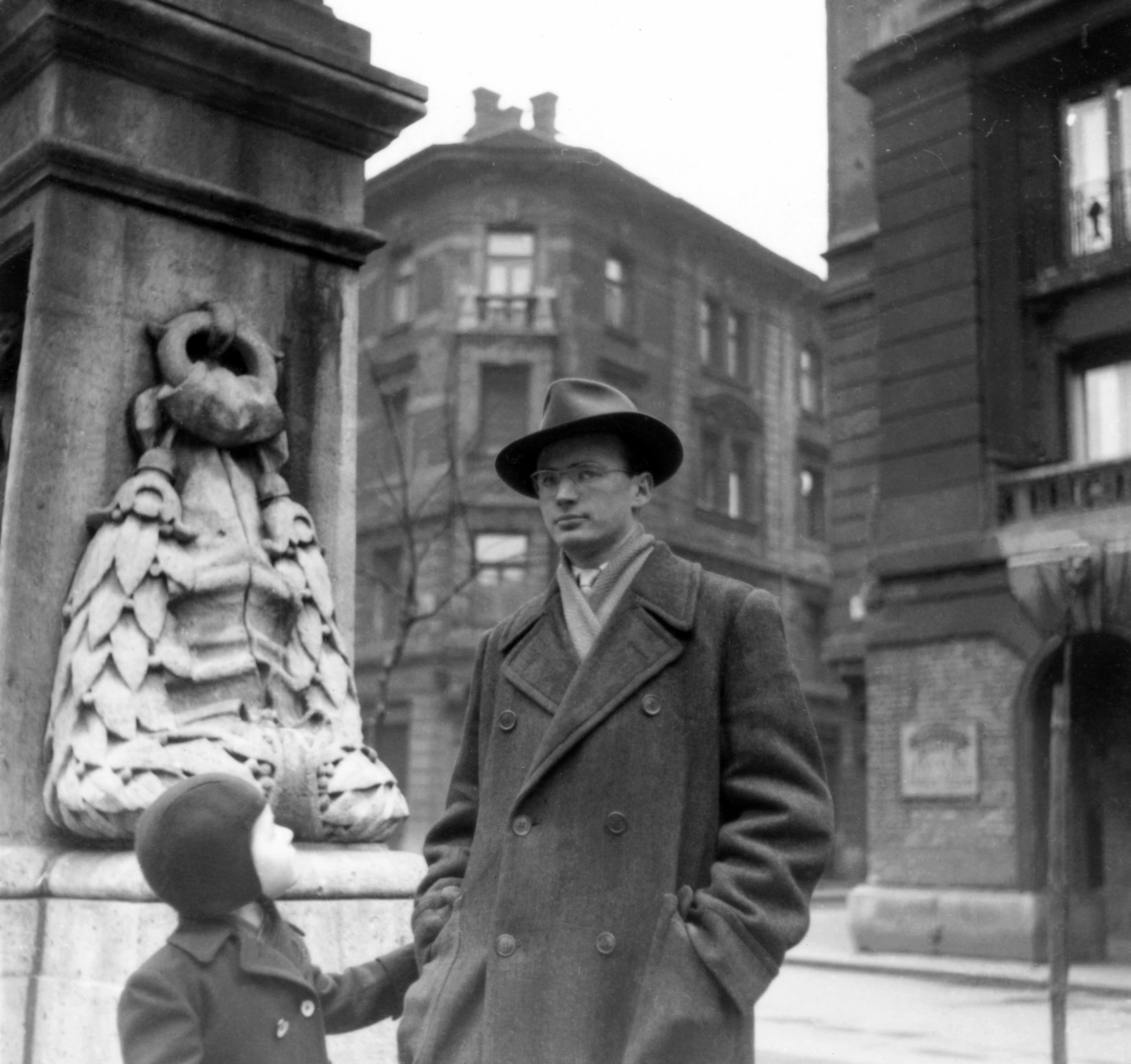 Hungary, Budapest VIII., Gutenberg tér, Fodor József szobrának talapzata, háttérben a Bródy Sándor utca - Mária utca sarok., 1959, Bartók István, hat, sculpture, glasses, kid, man, pedestal, double portrait, leather cap, Budapest, hands in pockets, double-breasted coat, Fortepan #31634