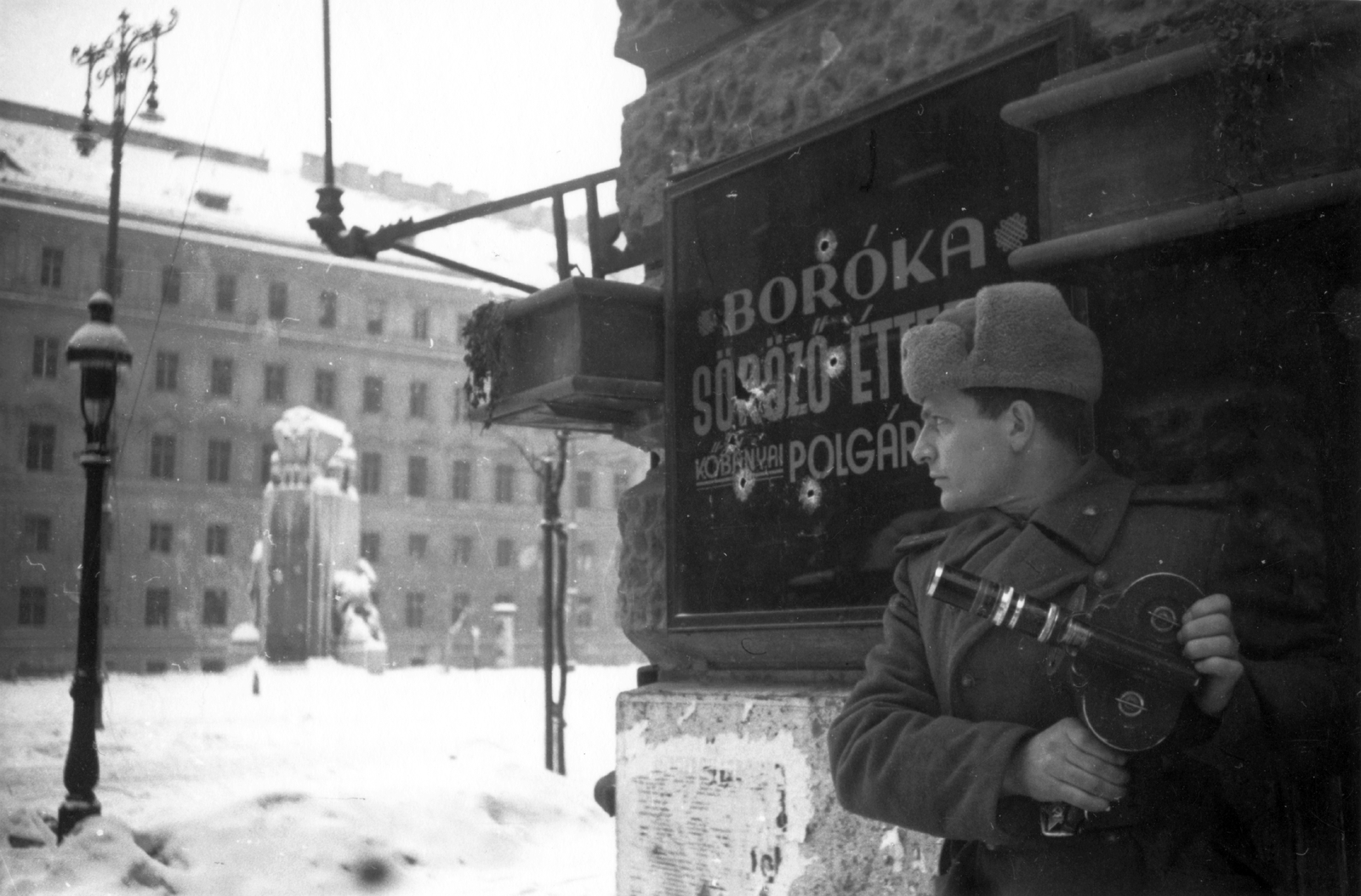 Hungary, Budapest V., Vértanúk tere a Nádor utcából nézve, szemben a Földművelésügyi Minisztérium épülete, középen a Nemzeti vértanúk emlékműve. Előtérben Julij Mihajlovics Kun operatőr haditudósító., 1945, Fortepan, filming, hospitality, winter, snow, sign-board, siege, second World War, Red Army, lamp post, movie camera, Budapest, fur hat, Fortepan #32050