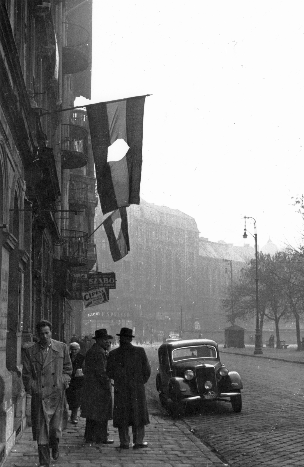 Hungary, Budapest VIII., II. János Pál pápa (Köztársaság) tér a Vay Ádám utca felől a Népszínház utca felé nézve., 1956, Pesti Srác2, flag, German brand, revolution, street view, genre painting, Mercedes-brand, lamp post, automobile, Mercedes-Benz 170V, shoemaker, tailors, symbol, Budapest, flag with a hole, Fortepan #32773