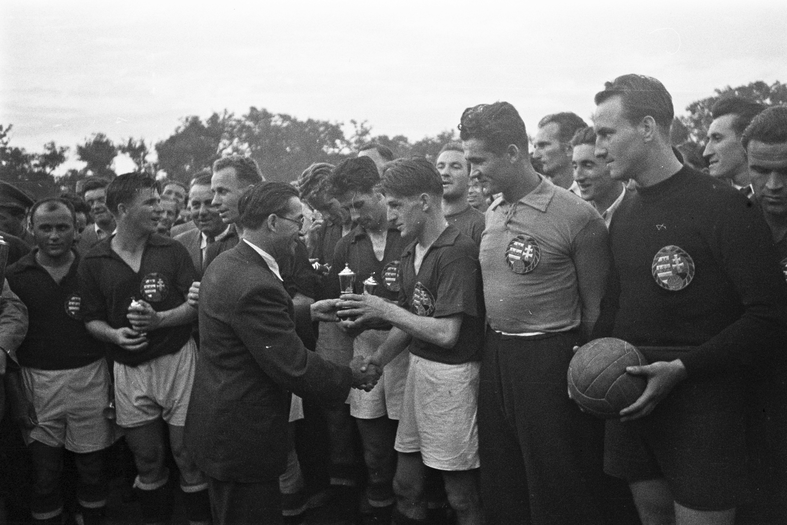 Hungary, Debrecen, Nagyerdei Stadion, a Magyarország - Lengyelország (8:2) válogatott labdarúgó-mérkőzés után Mazár Ferenc, a Népbolt NV vezérigazgatója adja át a mérkőzésre felajánlott serleg kicsinyített mását a győztes magyar csapatnak. A játékosok balról: Egresi, Puskás, Balogh II, Lantos, Bozsik, Czibor, Károlyi (tartalék kapus), Henni., 1949, Kovács Márton Ernő, celebrity, football, soccer team, handshake, Fortepan #32797