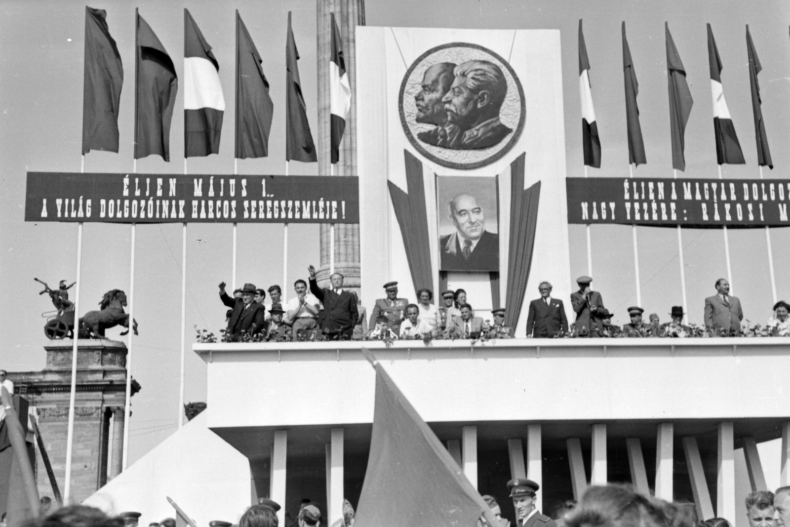 Hungary, Budapest XIV., Hősök tere, május 1-i dísztribün. Balra, kalapban Rákosi Mátyás, mögötte, ingben Marosán György, jobbra, rövid ujjú ingben Kovács István, mellette integet Vas Zoltán, a Rákosi kép alatt, zakóban Dobi István, tőle balra, ingben ül Rajk László, jobbra, egyenruhában ül Pálffy György, öltönyben áll Szakasits Árpád, tovább jobbra, egyenruhában Farkas Mihály, kettővel tovább öltönyben áll Nagy Imre., 1949, Kovács Márton Ernő, celebrity, personality cult, flag, Lenin-portrayal, political decoration, march, 1st of May parade, grandstand, Mátyás Rákosi-portrayal, Joseph Stalin portrayal, Budapest, politician, Fortepan #32919