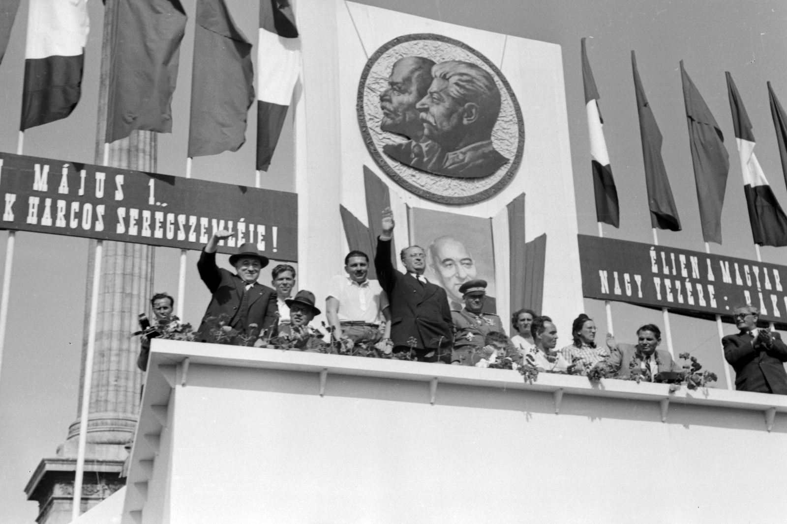 Hungary, Budapest XIV., Hősök tere, május 1-i dísztribün. Balra, kalapban Rákosi Mátyás, mögötte, ingben Marosán György, rövid ujjú ingben áll Kovács István, mellette öltönyben integet Vas Zoltán, középen, ingben ül Rajk László, mellette, zakóban Dobi István, a kép jobb szélén Szakasits Árpád., 1949, Kovács Márton Ernő, celebrity, personality cult, flag, Lenin-portrayal, political decoration, 1st of May parade, grandstand, Mátyás Rákosi-portrayal, Joseph Stalin portrayal, Budapest, politician, Fortepan #32920