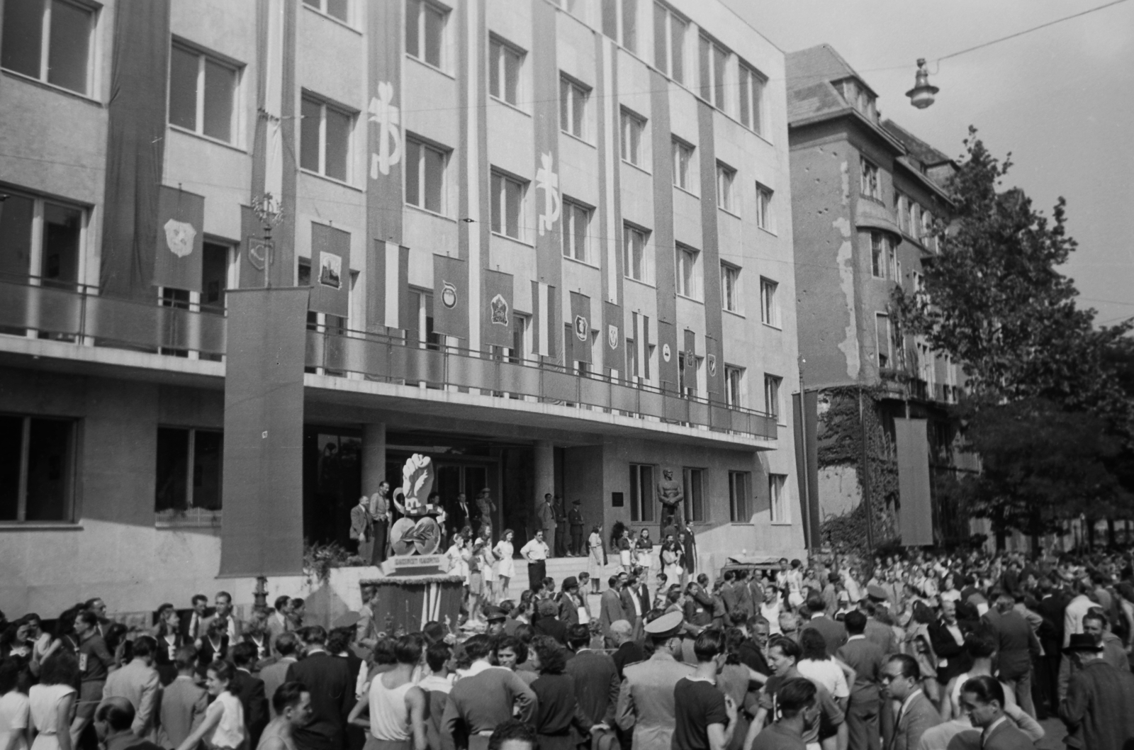 Hungary, Budapest VI., Dózsa György út 84., Béke staféta a SZOT székház előtt. A bejárat lépcsőjének jobb oldalánál Bokros Birman Dezső szobrászművész alkotása, a Vasmunkás szobra, melyet a székház 1948. augusztus 1-i megnyitása alkalmával lepleztek le., 1949, Kovács Márton Ernő, Budapest, sculpture, festive, socialism, union, Fortepan #33250