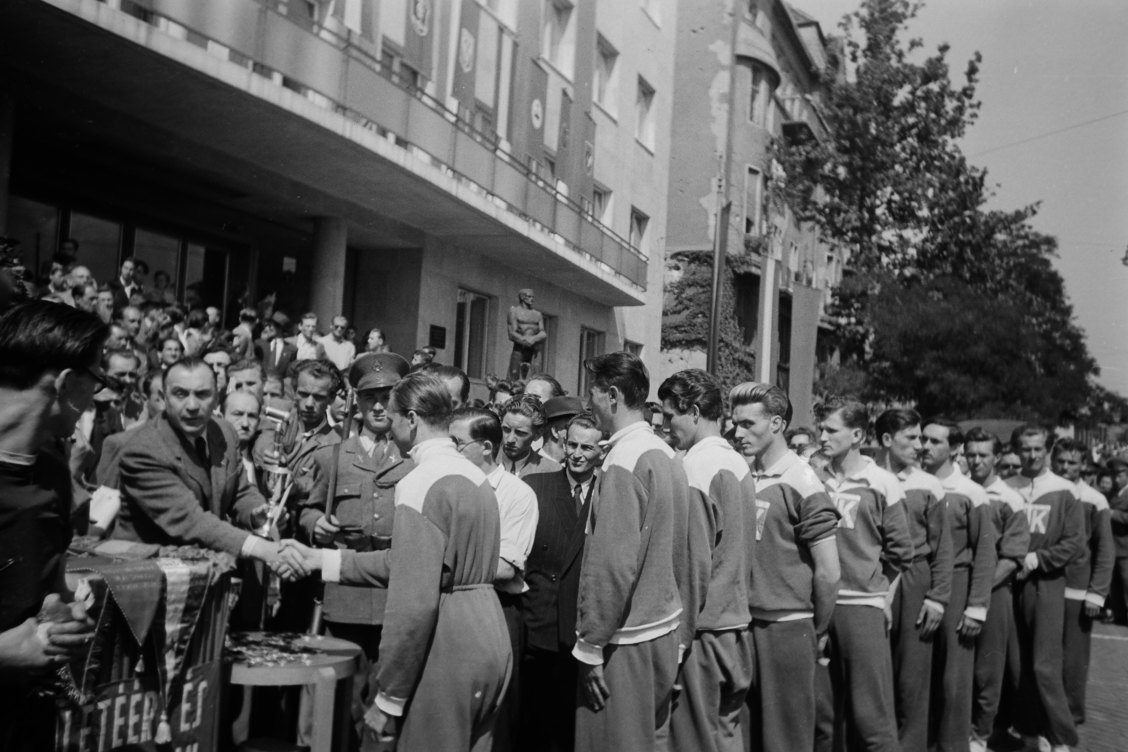 Hungary, Budapest VI., Dózsa György út 84., a SZOT székház előtt Sebes Gusztáv a Béke staféta kupát és érmeket ad át az MTK sportolóinak. A kép közepén Bokros Birman Dezső szobrászművész alkotása, a Vasmunkás szobra, melyet a székház 1948. augusztus 1-i megnyitása alkalmával lepleztek le., 1949, Kovács Márton Ernő, Budapest, youth, festive, socialism, union, Fortepan #33254