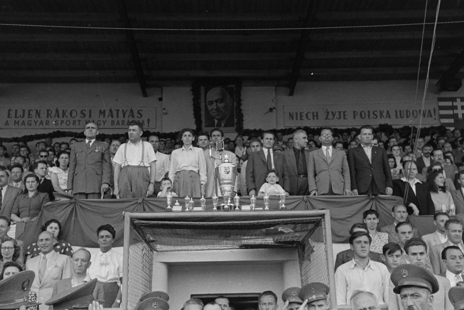 Hungary, Debrecen, Nagyerdei Stadion, Magyarország - Lengyelország (8:2) válogatott labdarúgó-mérkőzés. A dísztribünön jobbról az első Zsofinyecz Mihály nehézgépipari miniszter, második Kállai Gyula külügyminiszter, harmadik Ménes János Debrecen polgármestere, negyedik Simon Lajos Budapest alpolgármestere, mögötte Köböl József  Nagy-Budapest törvényhatóságának elnöke, balról a második Kossa István pénzügyminiszter., 1949, Kovács Márton Ernő, celebrity, political decoration, Mátyás Rákosi-portrayal, cup, Fortepan #33538