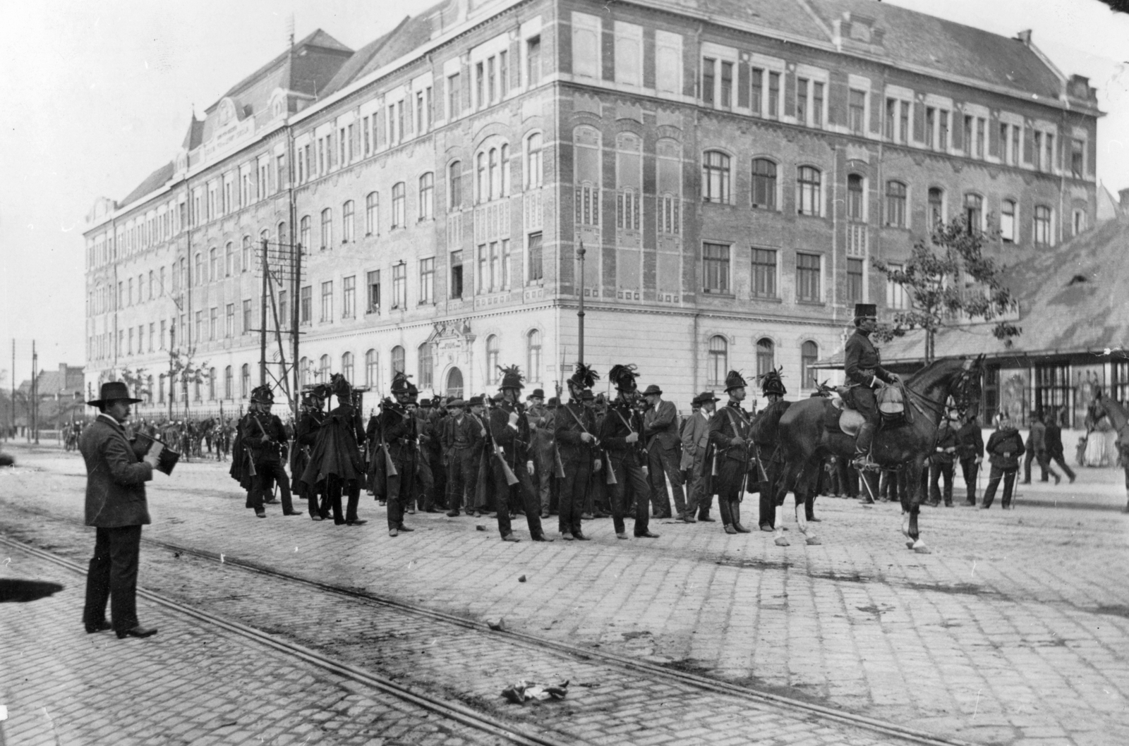 Magyarország, Budapest XIII., a Váci út - Janicsár utca sarkán a Váci úti elemi iskola. Előtérben csendőrök őrzik a Vérvörös csütörtökön elfogott tüntetőket. Balra Balogh Rudolf fotóművész áll, a felvételt a Vasárnapi Újság másik riportere Jelfy Gyula készítette 1912. május 23-án., 1912, Angyalföldi Helytörténeti Gyűjtemény, iskola, tömeg, csendőr, fegyver, fényképezőgép, tüntetés, puska, lovasrendőr, Budapest, Mannlicher M95, híres ember, sínpálya, Fortepan #39727