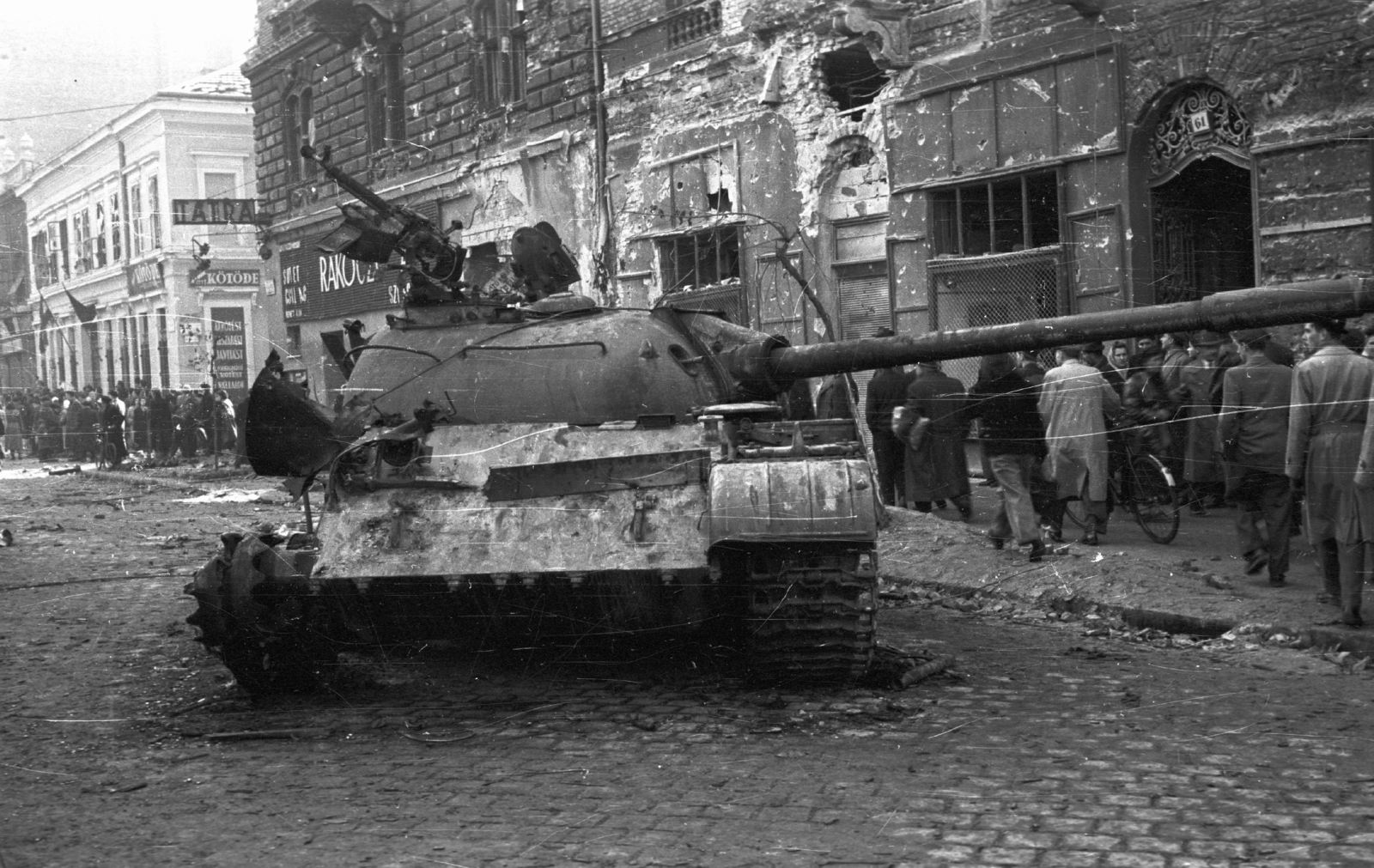 Hungary, Budapest IX., Üllői út, kilőtt szovjet T-54-es harckocsi a 61-es számú ház előtt. Háttérben a Berzenczey utca sarkánál a Tátra (később Balaton) mozi látható., 1956, Nagy Gyula, war damage, sign-board, Soviet brand, revolution, tank, wreck, damaged building, machine gun, combat vehicle, Budapest, Fortepan #39836