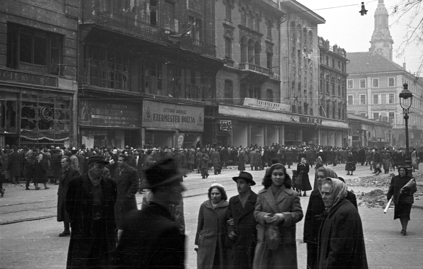 Hungary, Budapest V., Kossuth Lajos utca a Semmelweis utca felől a Ferenciek tere (Felszabadulás tér) felé nézve., 1956, Nagy Gyula, war damage, sign-board, mass, revolution, pedestrian, street view, lamp post, store, store display, gas lamp, standing in line, trash can, Budapest, Fortepan #39966