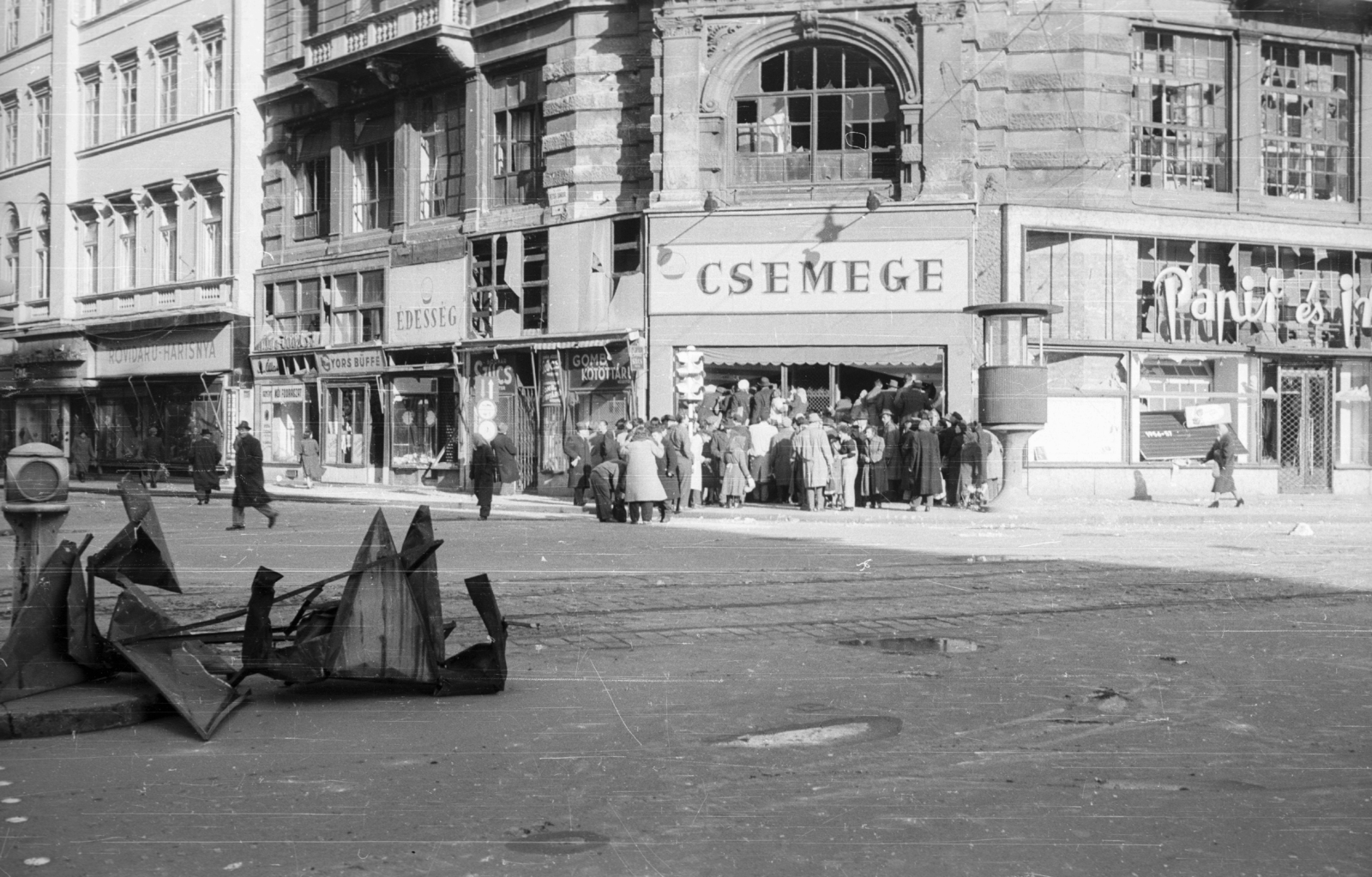Hungary, Budapest V., Ferenciek tere (Felszabadulás tér), Kossuth Lajos utca - Petőfi Sándor utca sarok., 1956, Nagy Gyula, sunshine, war damage, sign-board, revolution, street view, store display, csibi lamp, damaged building, Budapest, Fortepan #39972