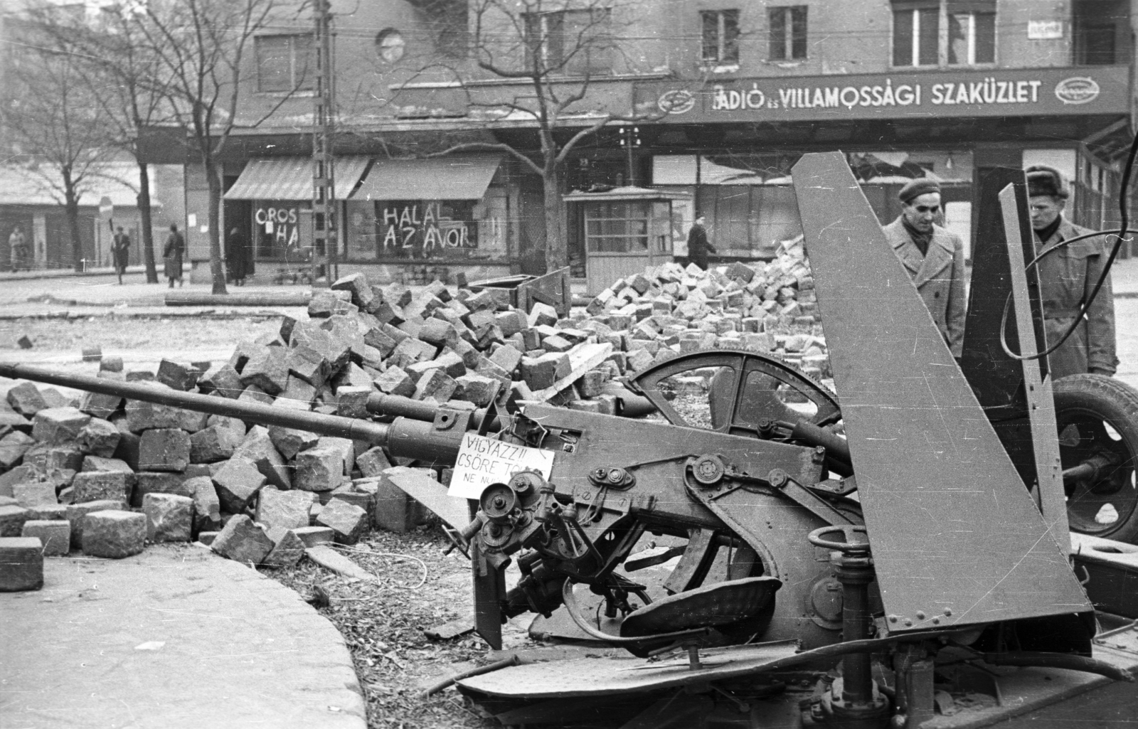 Magyarország, Budapest XI., Fehérvári út, szemben a Vásárhelyi Pál utca torkolata, jobbra a Móricz Zsigmond körtér, a Váli utca sarkáról nézve., 1956, Nagy Gyula, cégtábla, felirat, forradalom, barikád, fegyver, kockakő, gépágyú, Budapest, Fortepan #40035