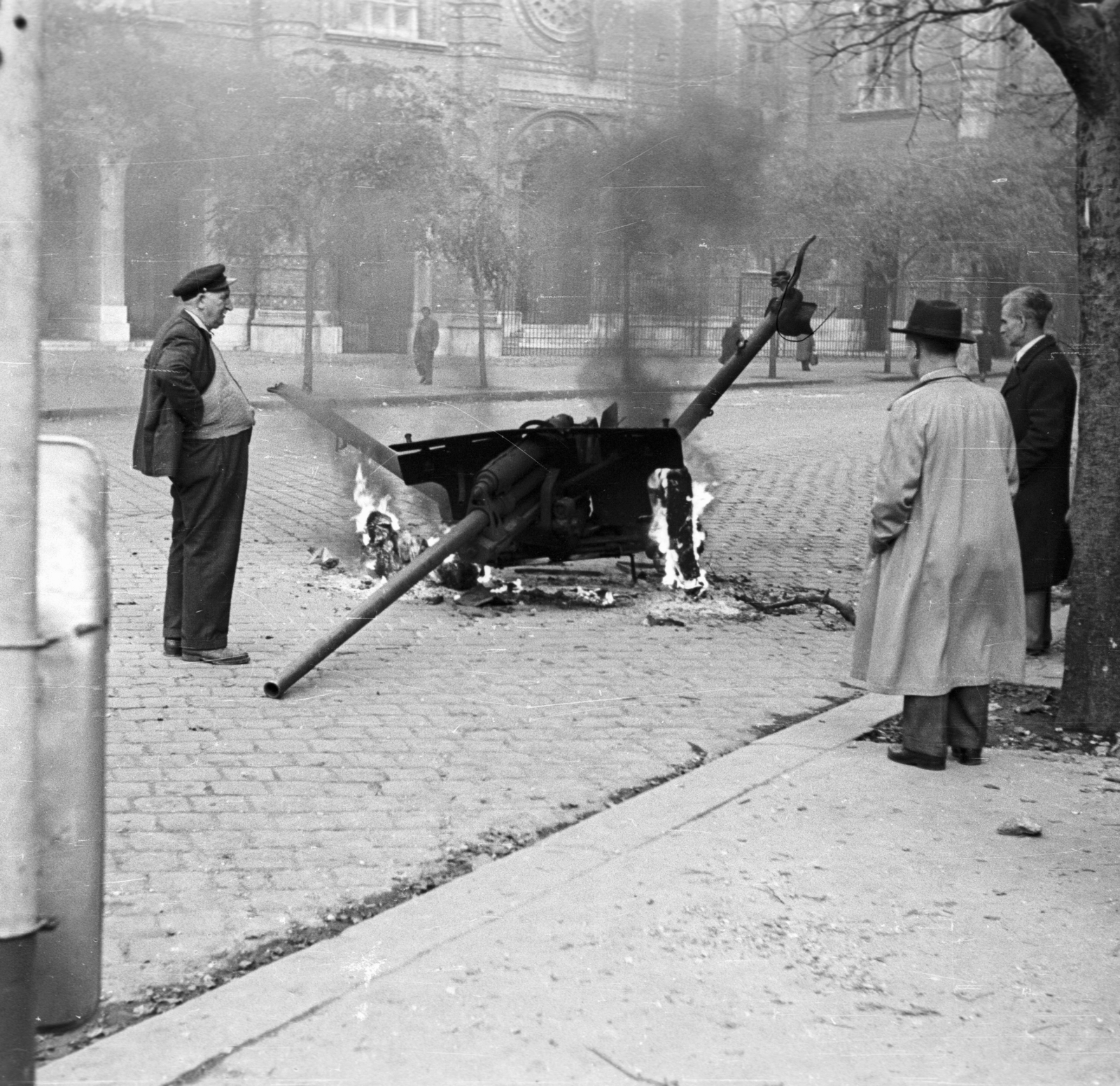 Hungary, Budapest VII., Dohány utca eleje, szemben a Zsinagóga, az előtérben lángoló páncéltörő ágyú., 1956, Nagy Gyula, hat, revolution, synagogue, cannon, weapon, trench coat, ordnance, judaism, Budapest, Fortepan #40056