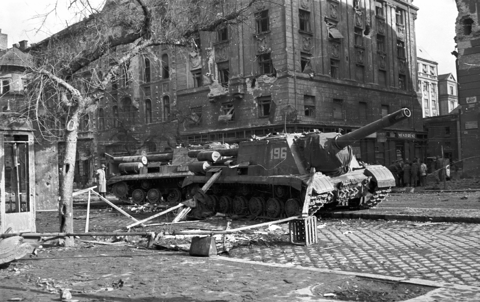 Hungary, Budapest VIII., a József körút a Corvin (Kisfaludy) köznél. Harcképtelenné tett ISZU-152-es szovjet rohamlövegek., 1956, Nagy Gyula, war damage, Soviet brand, revolution, street view, wreck, phone booth, damaged building, ordnance, combat vehicle, ISU-152 assault gun, Budapest, Fortepan #40173
