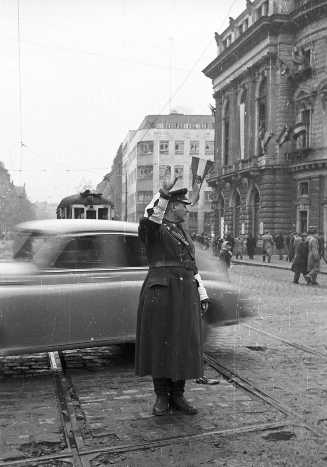 Magyarország, Budapest VIII.,Budapest VII., Rákóczi út - Nagykörút kereszteződés. Háttérben a Nemzeti Színház és a Szabad Nép székháza., 1956, Nagy Gyula, közlekedés, zászló, forradalom, nemzeti színház, rendőr, villamos, Fellner és Helmer-terv, eklektikus építészet, Budapest, forgalomirányítás, Fortepan #40247