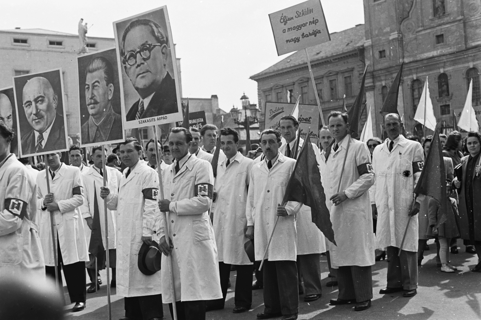 Hungary, Győr, Széchenyi tér, balra az egykori Lloyd székház, előtte a Mária oszlop részlete, jobbra a Szent Ignác bencés templom. A Népbolt dolgozói a május 1-i felvonuláson., 1949, Konok Tamás id, march, 1st of May parade, Mátyás Rákosi-portrayal, Joseph Stalin portrayal, Árpád Szakasits portrayal, armband, people's store, Fortepan #43043