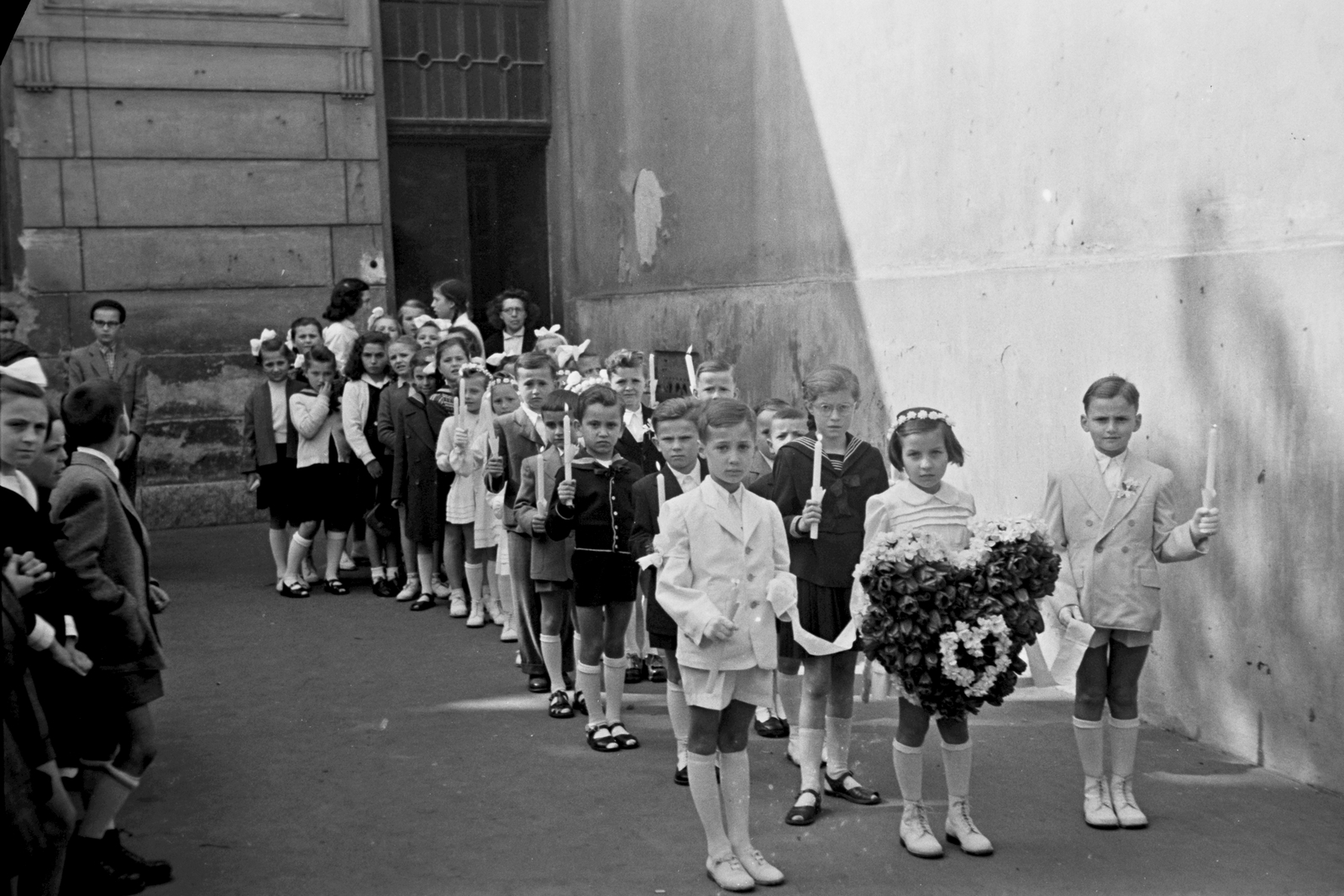 Magyarország, Győr, Bécsi kapu (Erzsébet) tér, jobbról a Kapucinus templom oldalhomlokzata, elsőáldozók, 1947, Konok Tamás id, gyermek, gyertya, virág, elsőáldozás, ünneplő ruha, Fortepan #43329