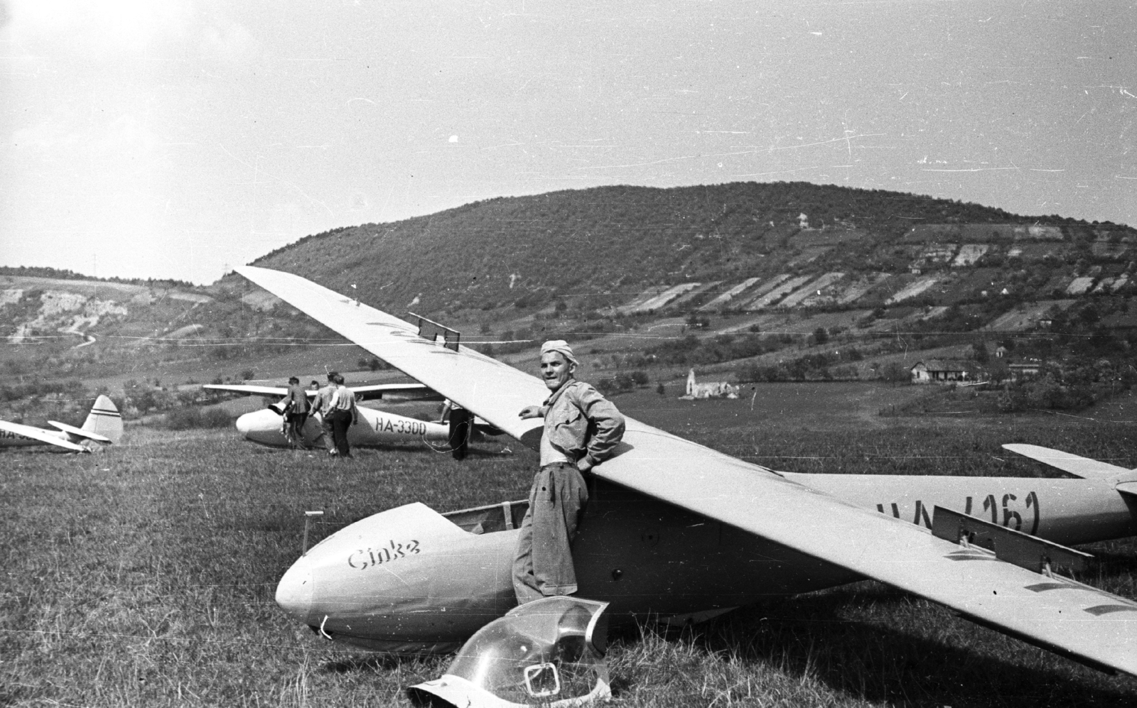 Hungary, Hármashatárhegy Airport, Budapest II., C-2 Cinke vitorlázó repülőgép, előtte Durucz Jenő (MALÉV-kapitány) oktató. Takarásban egy Rubik R 08 D-Pilis. Távolban a Csúcs-hegy, előtte a Gercsei (vagy Gercsényi) templomrom., 1957, Mészáros Zoltán, Hungarian brand, airport, sailplane, Budapest, Fortepan #44934