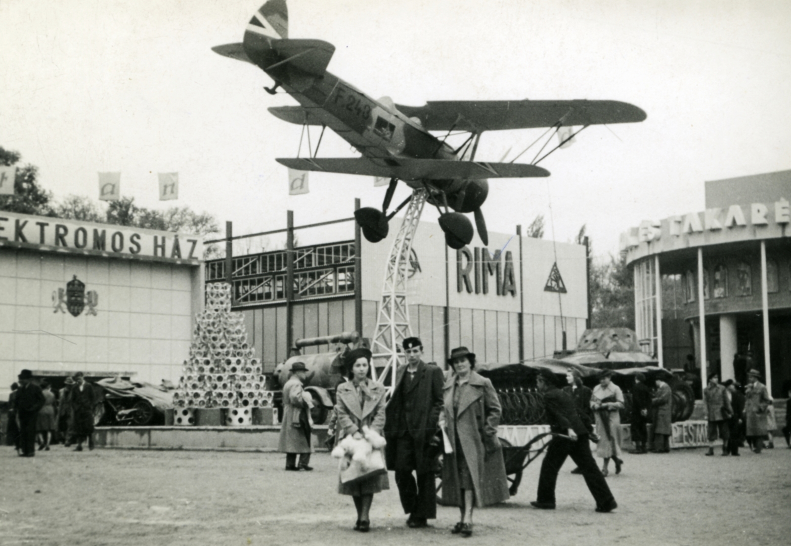 Magyarország, Városliget,Budapesti Nemzetközi Vásár, Budapest XIV., a Weiss Manfréd Acél- és Fémművek kiállítási területe. Az állványon WM-21 Sólyom közelfelderítő repülőgép., 1940, Morvay Kinga, kalap, magyar gyártmány, repülőgép, nemzetközi vásár, diáksapka, Weiss Manfréd-márka, Weiss Manfréd WM-21 Sólyom, biplán, Budapest, Rimamurány-Salgótarjáni Vasmű Rt, Fortepan #45395