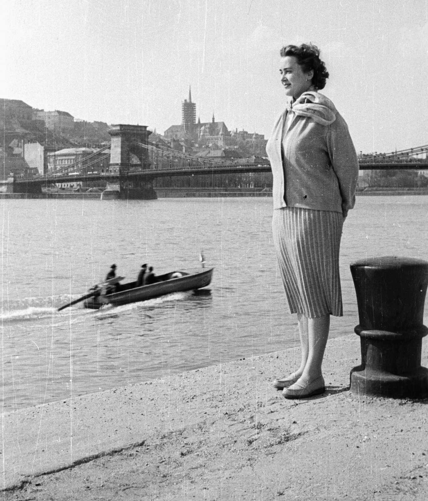 Magyarország, Budapest V., pesti alsó rakpart, háttérben a Széchenyi Lánchíd és a felállványozott Mátyás-templom., 1957, Nagy Gyula, divat, motorcsónak, sál, Kováts csónakmotor, rohamcsónak, Budapest, függőhíd, William Tierney Clark-terv, Fortepan #50494