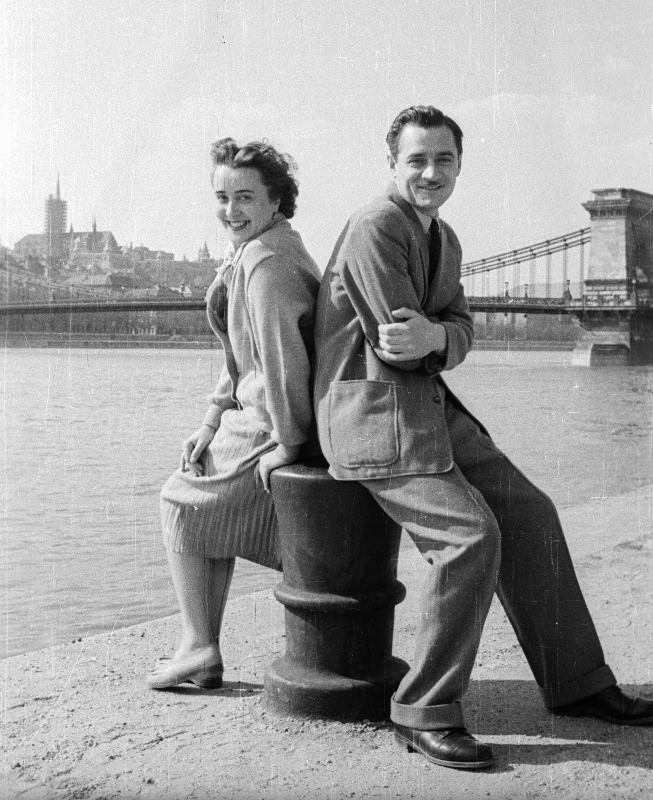 Hungary, Budapest V., pesti alsó rakpart, háttérben a Széchenyi Lánchíd és a felállványozott Mátyás-templom., 1957, Nagy Gyula, smile, man and woman, Budapest, suspension bridge, William Tierney Clark-design, mooring bollard, Fortepan #50495