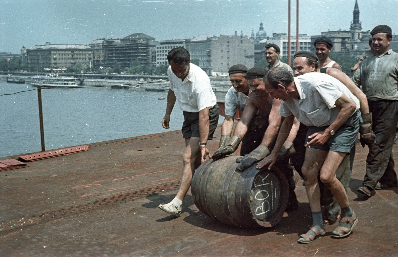 Hungary, Budapest V., az Erzsébet híd építése, hordógurítás a szerkezetkész állapot ünneplésekor, háttérben a Dunakorzó épületei. A felvétel 1964. július 15-én készült., 1964, Nagy Gyula, colorful, festive, barrel, Budapest, Duna-bridge, socks and sandal, Fortepan #50570