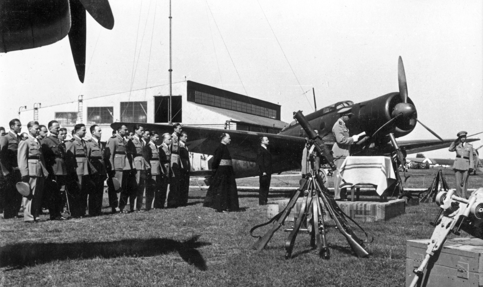 Hungary, Kecskemét, repülőtér, eskütétel. Háttérben az 1/2. távolfelderítő század gépe, Heinkel He-70K típusú távolfelderítő repülőgép és az 1. sz. Hangár., 1940, Fortepan, German brand, priest, airplane, Royal Hungarian Air Force, soldier, airport, Heinkel-brand, gun, machine gun, Schwarzlose-brand, Fortepan #52475