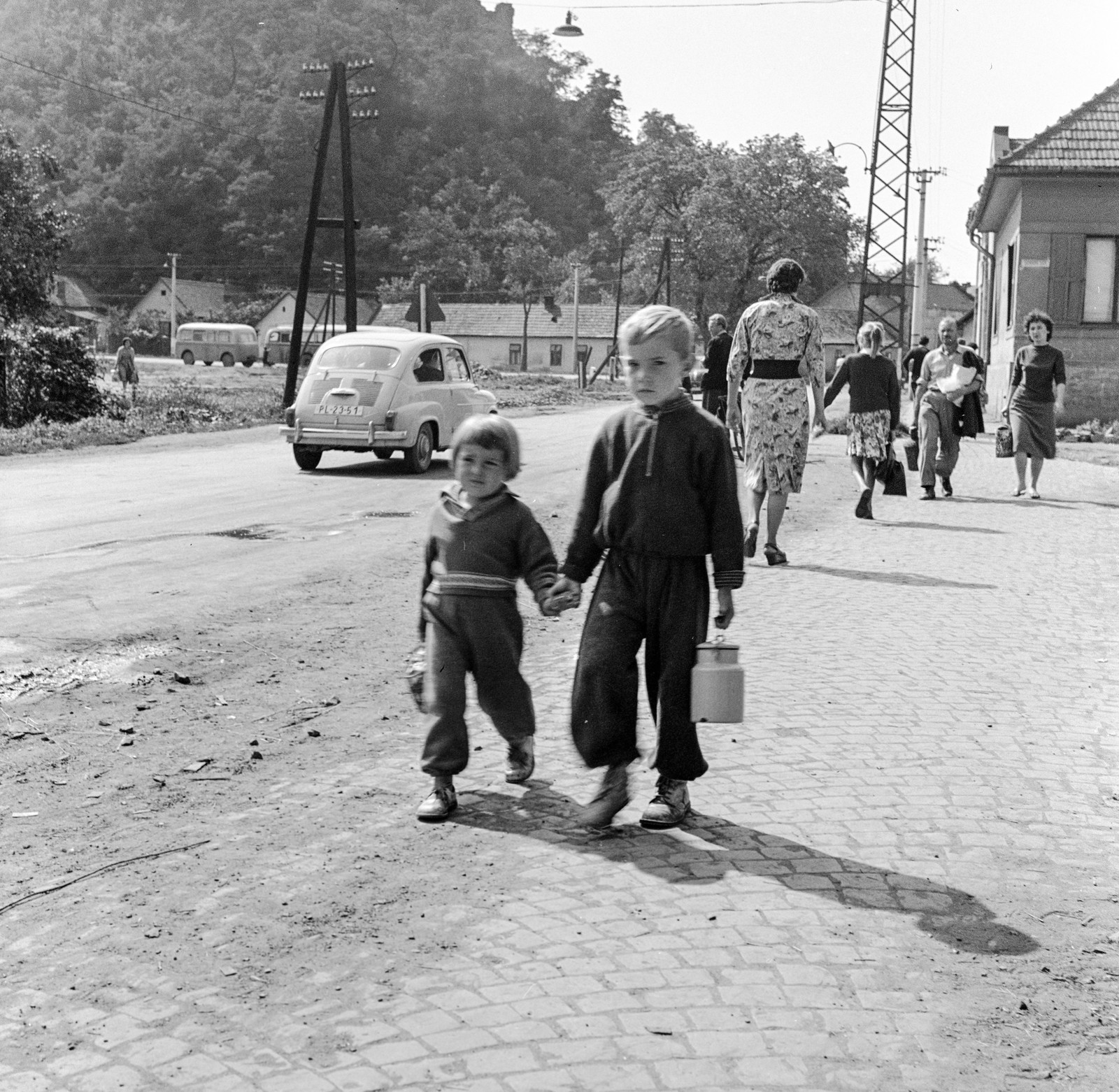 Slovakia, Fiľakovo, ulica Továrenska (Gyári utca), balra a várhegy., 1960, Zsanda Zsolt, Vajszada Károly, Czechoslovakia, Yugoslavian brand, Zastava-brand, street view, kids, cobblestones, automobile, number plate, milk can, hold hands, Fortepan #53950