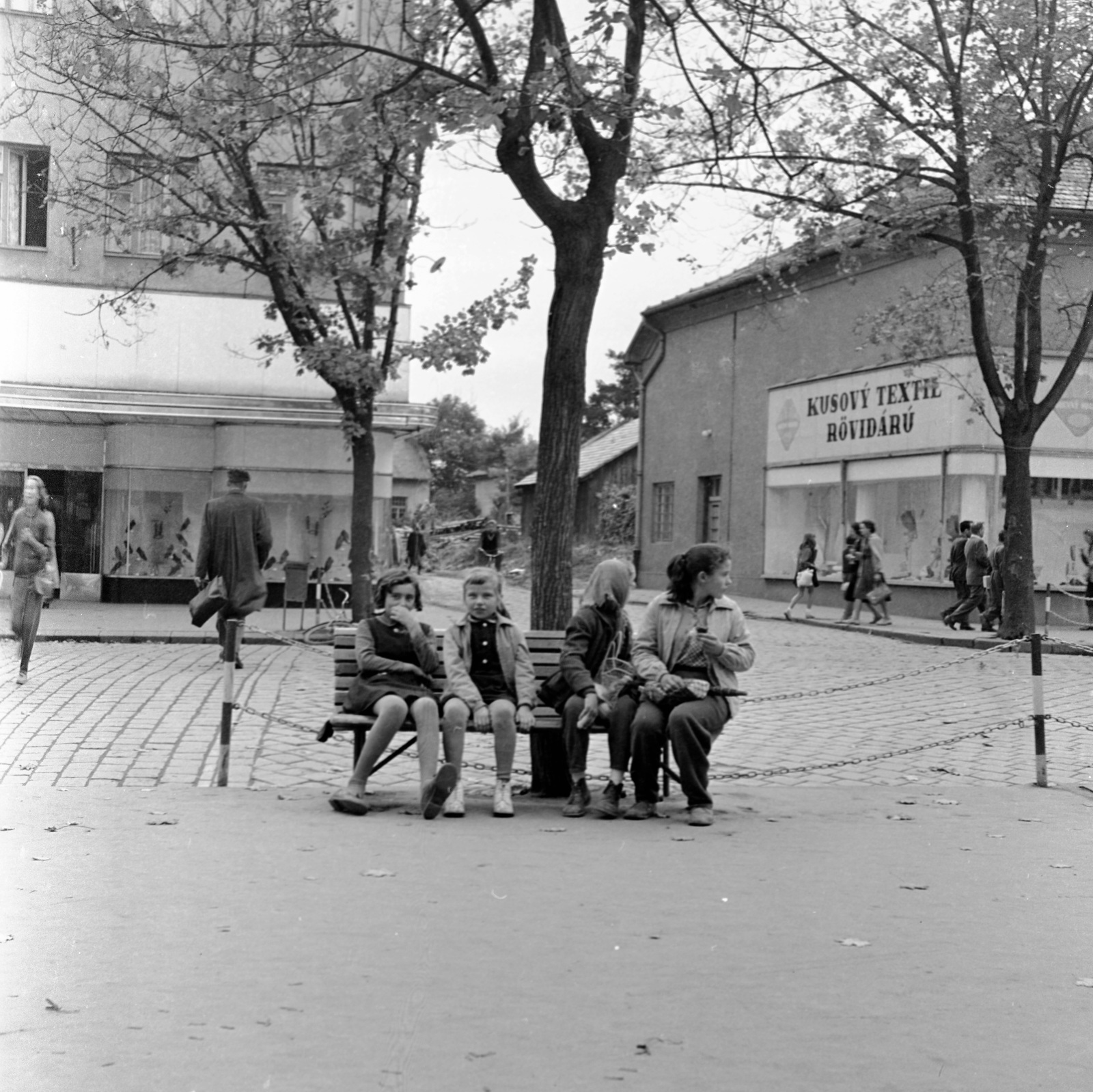 Slovakia, Lučenec, ulica Tomása Garrigue Masaryka, szemben az ulica Jána Amosa Komenského torkolata., 1960, Zsanda Zsolt, Vajszada Károly, Czechoslovakia, bench, clothing store, bilingual sign, Fortepan #54002