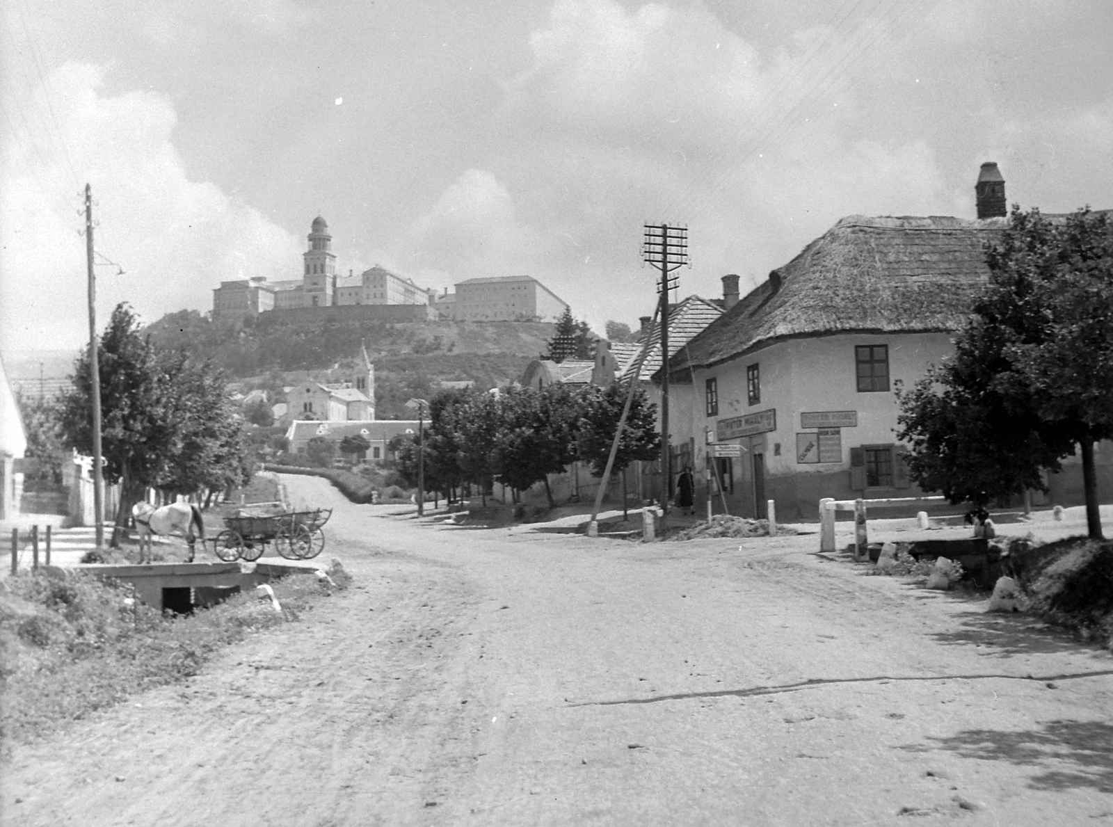 Magyarország, Pannonhalma, (Győrszentmárton), Szabadság tér, szemben a Gyümölcsoltó Boldogasszony-templom és plébánia. A Szent Márton-hegyen a Pannonhalmi Bencés Főapátság., 1948, Gyöngyi, vallás, szekér, lovaskocsi, utcakép, nádtető, üzletportál, bencés rend, Fortepan #5467