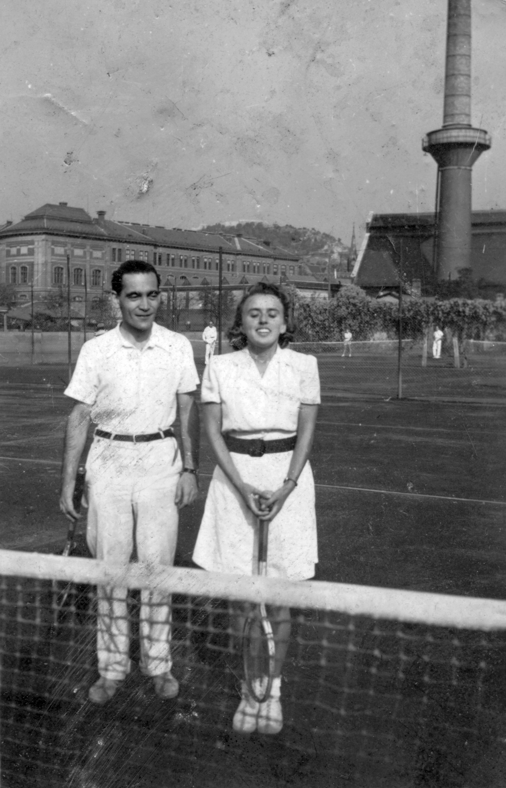 Hungary, Budapest XI., Stoczek József (Stoczek) utca, a MAFC sporttelep teniszpályája. Háttérben az egyetem kazántelepének (mára visszabontott) kéménye., 1941, Saly Noémi, men, chimney, woman, tennis court, double portrait, tennis rackets, Budapest, Fortepan #55071