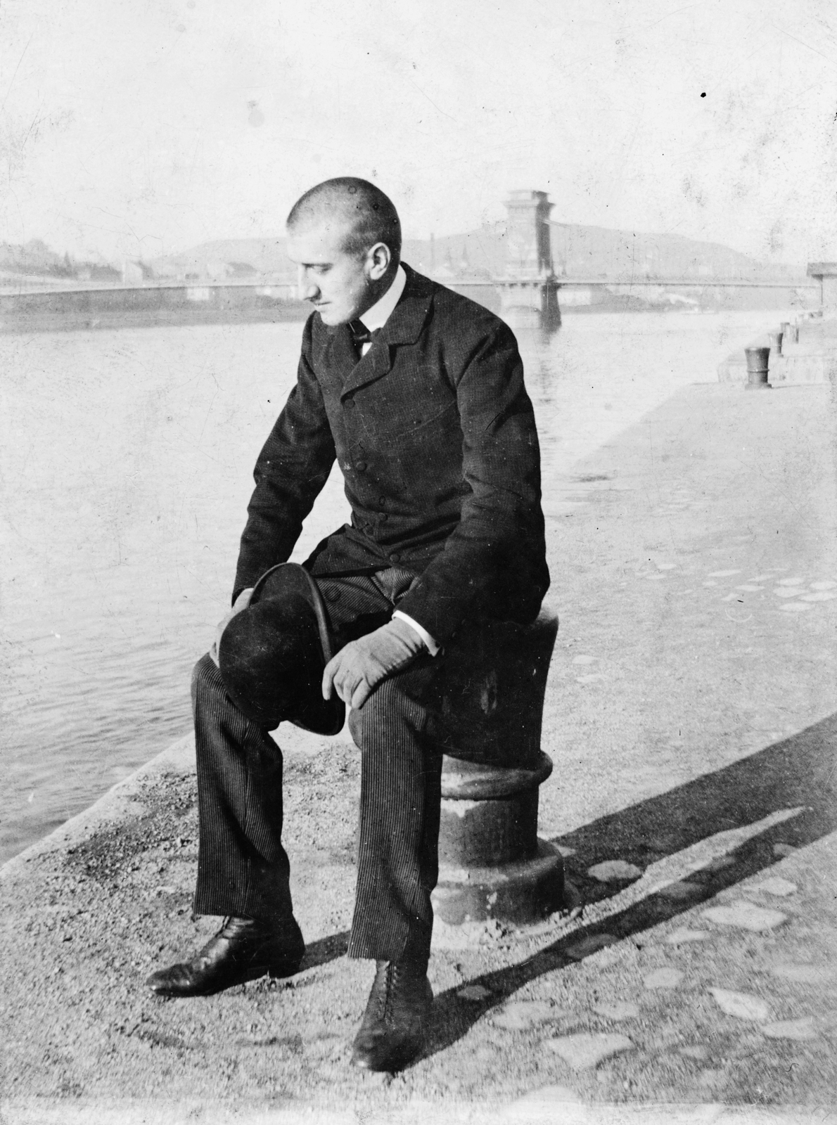 Hungary, Budapest V., Siklóssy László a pesti alsó rakparton, háttérben a Széchenyi Lánchíd., 1900, Magyar Bálint, portrait, celebrity, bridge, man, bowler hat, mooring bollard, Budapest, suspension bridge, William Tierney Clark-design, hat in hand, Fortepan #55376