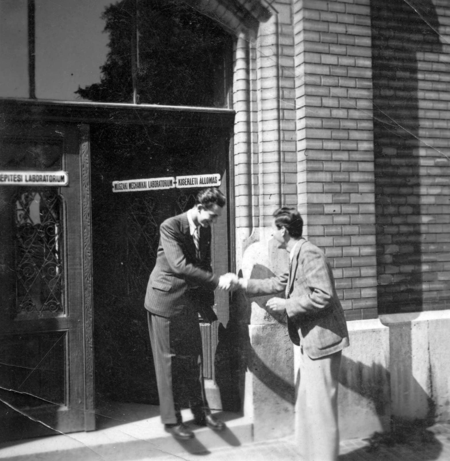 Hungary, Budapest XI., Műegyetem rakpart, a Magyar királyi József nádor Műszaki és Gazdaságtudományi Egyetem (később Budapesti Műszaki és Gazdaságtudományi Egyetem) Műszaki Mechanikai épületének bejárata., 1941, Botár Angéla, label, gate, men, fun, building, handshake, Budapest, Budapest University of Technology, enamel sign, Fortepan #57896