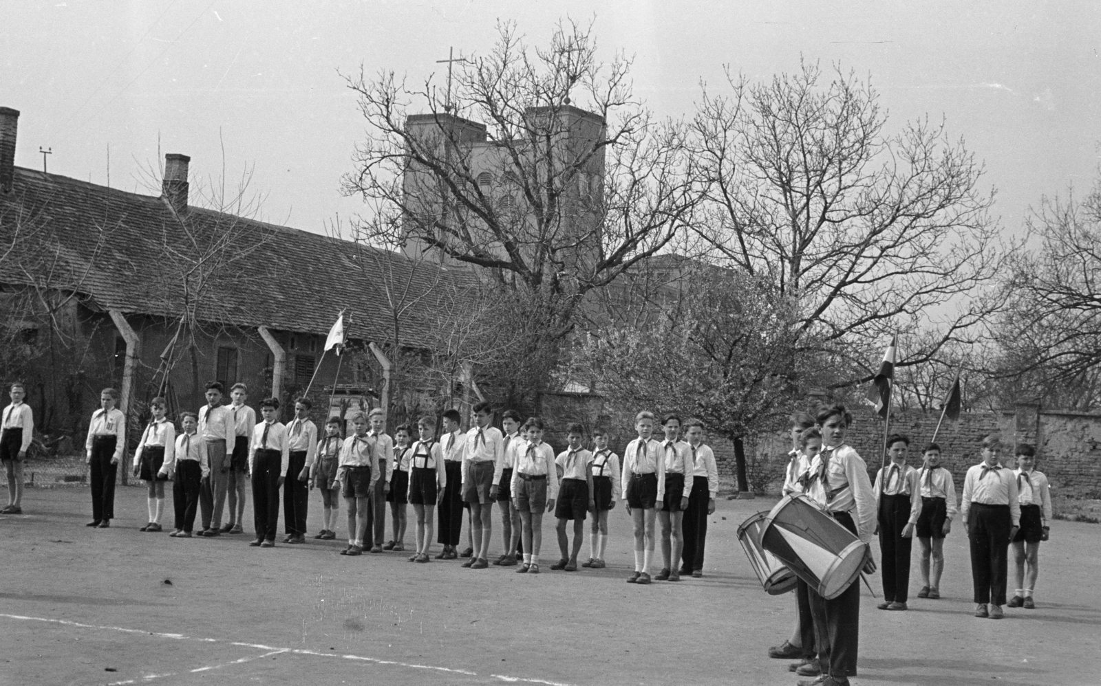 Magyarország, Csorna, Árpád utca, általános iskola udvara. Háttérben a Jézus Szíve-templom., 1958, Lipovits Károly, úttörő, zászló, ünnepség, dob, Fortepan #61794