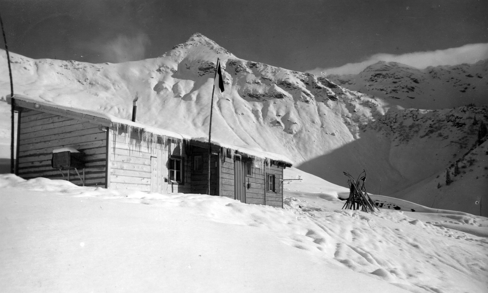 Ausztria, Aurach bei Kitzbühel, Hochwildalmhütte, a menedékház mögött a hegycsúcs a Bischof (2127 m)., 1931, A R, tél, hó, zászló, hegy, füst, síléc, zászlórúd, menedékház, jégcsap, Fortepan #62306