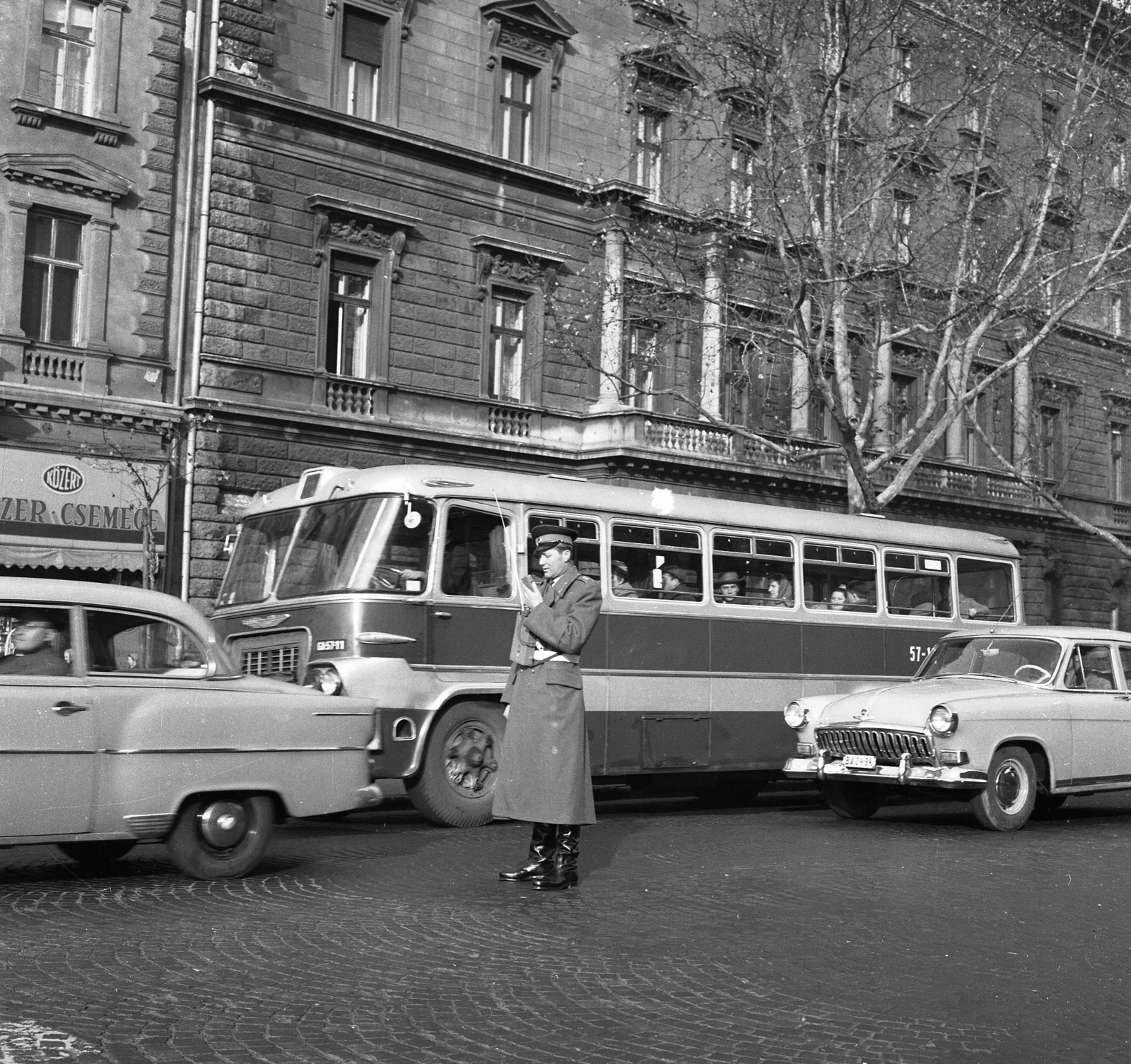 Hungary, Budapest VI., Andrássy út (Népköztársaság útja) az Oktogonnál (November 7. tér), szemben az 52. szám a Hagenmacher-ház., 1963, Magyar Rendőr, traffic, bus, sign-board, street view, Ikarus 620, automobile, M21 Wolga, transceiver, Budapest, grocery store, Közért Company, Fortepan #65004