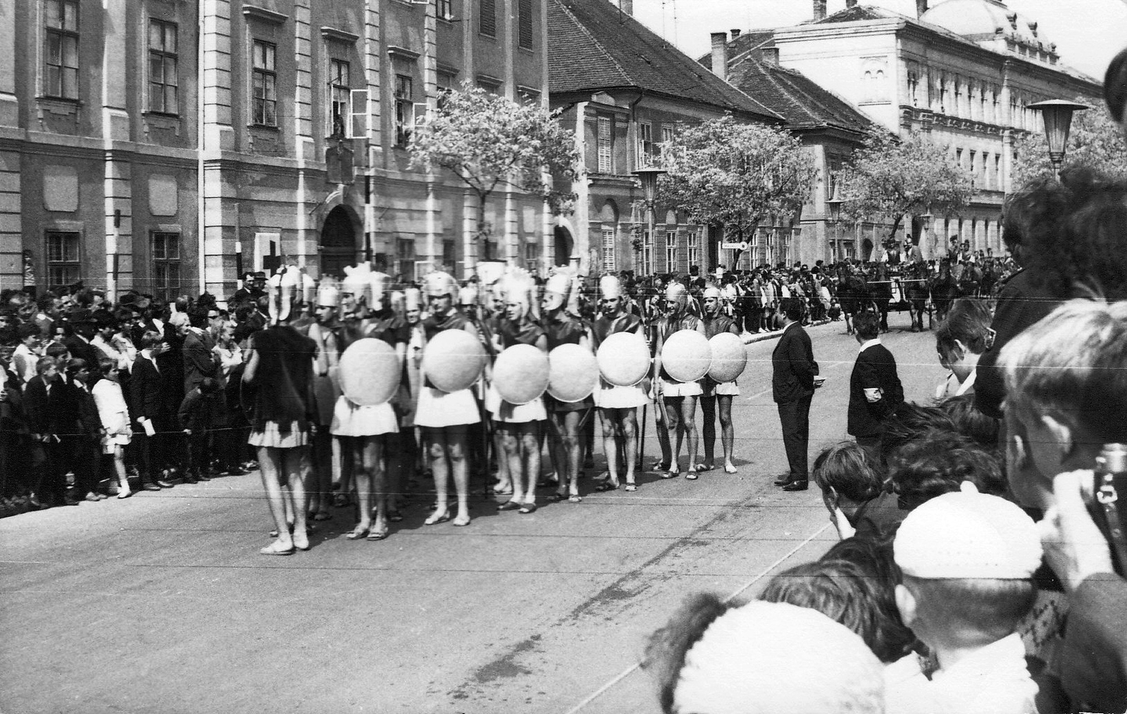 Magyarország, Szombathely, Szily János (Alkotmány) utca, a Savaria Történelmi Karnevál résztvevőinek felvonulása a Mindszenty József (Templom) tér közelében. Háttérben balra a Savaria Gimnázium és Középiskolai Leánykollégium (később Egyházmegyei Könyvtár és a Brenner János Kollégium) épülete, jobbra a Szombathelyi Törvényszék épülete., 1967, Kelemen Zoltán, utcakép, felvonulás, jelmez, közönség, Fortepan #69949