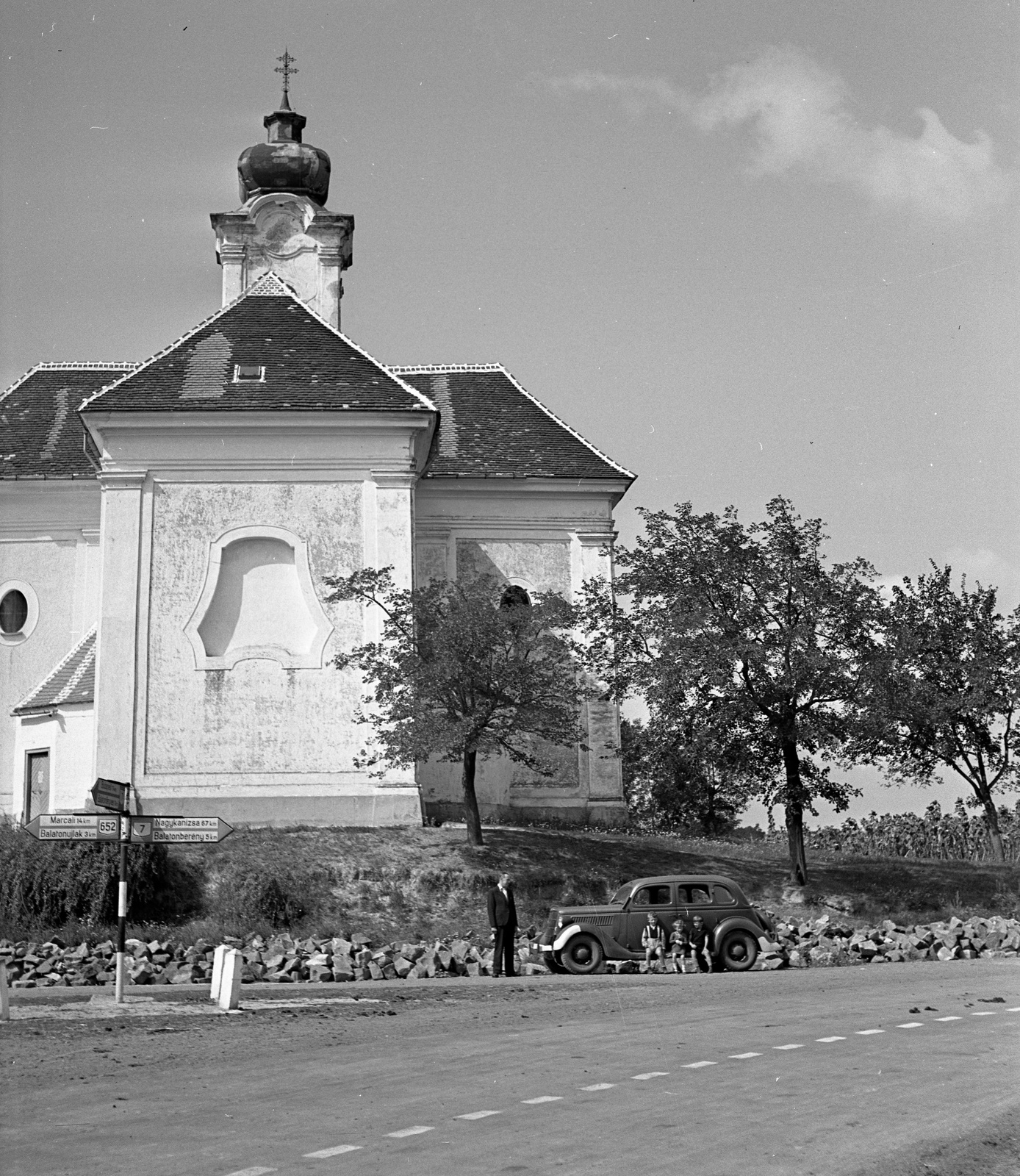 Hungary, Balatonkeresztúr, Ady Endre utca a 7-es főút elágazásánál, a katolikus templom előtt egy Ford V8 Modell 48, 1935-ös kiadású személygépkocsi., 1943, Lissák Tivadar, church, american brand, road signs, Ford-brand, automobile, sitting on a car, Fortepan #72488