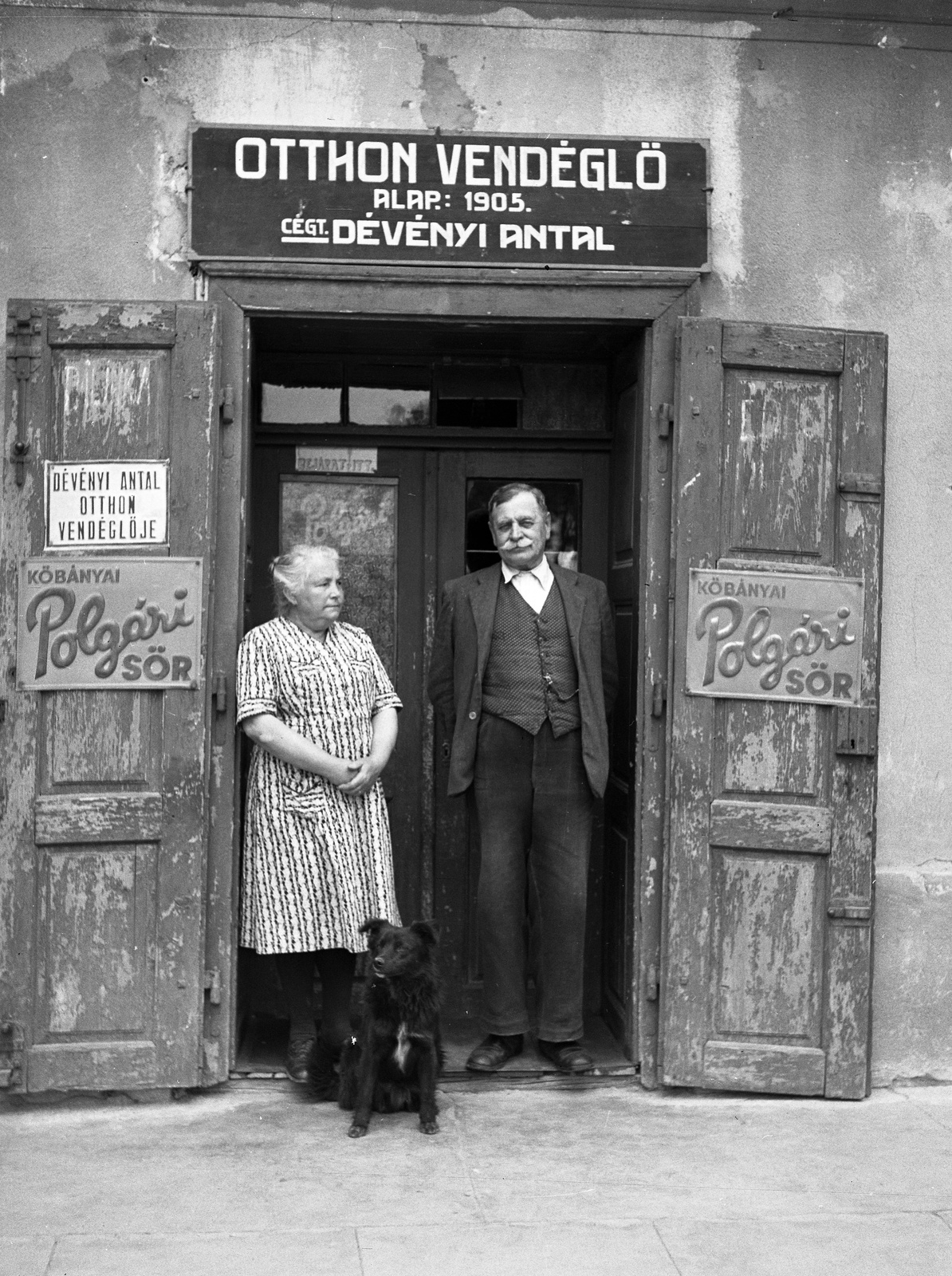 Magyarország, Bicske, Kossuth Lajos tér (Vásártér). Az Otthon vendéglő tulajdonosa feleségével., 1946, Lissák Tivadar, reklám, kutya, vendéglő, cégtábla, üzletportál, ajtóban állás, Fortepan #73006