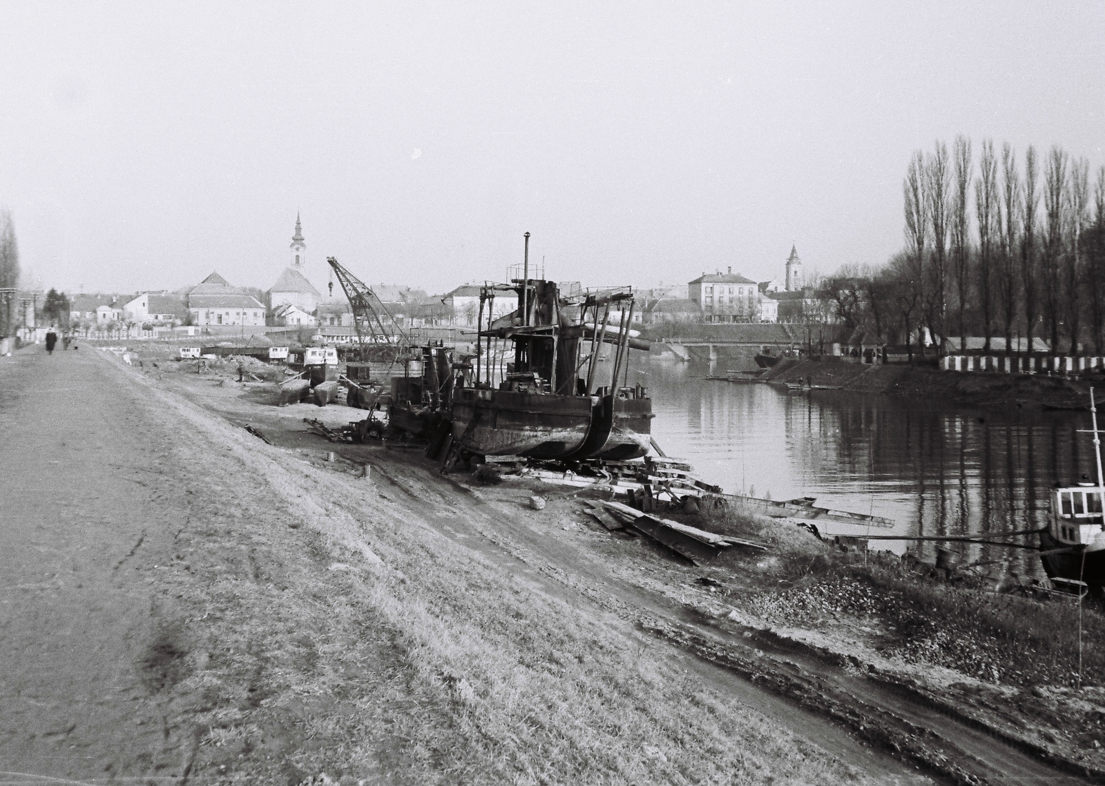 Hungary, Baja, a Sugovica (Kamarás-Duna) partja. A háttérben balra a Szent Péter és Pál apostolok templom, jobbra a Páduai Szent Antal-templom tornya. Előtérben az 1982-ben felrobbantott szigeti híd, jobbra a Petőfi-sziget., 1963, Márton Gábor, ship, dredge, Fortepan #73623