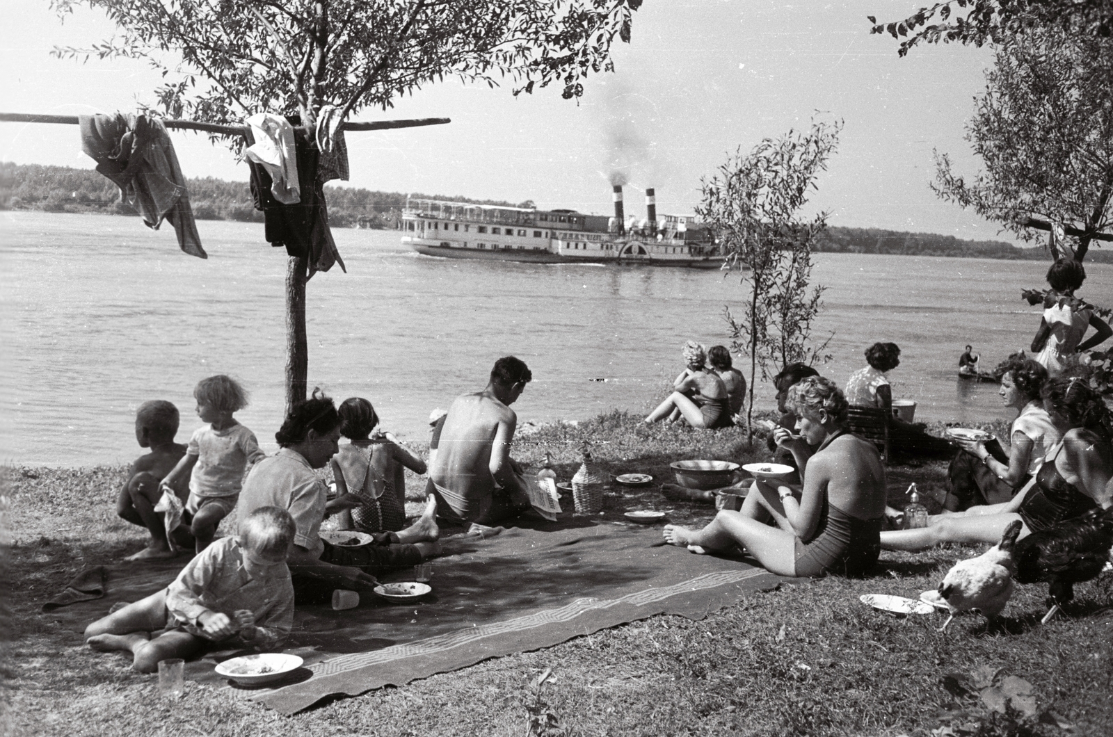 Hungary, Érsekcsanád, Duna-part a révcsárda felett. Szemben a Szent István gőzhajó mögött a Veránkai-Duna bejárata., 1960, Márton Gábor, free time, ship, bathing suit, river, meal, poultry, wrist watch, picnic, summer, boat, man, shore, steamboat, soda water bottle, blanket, demijohn, Szent István/Queen Zita ship, Fortepan #73640