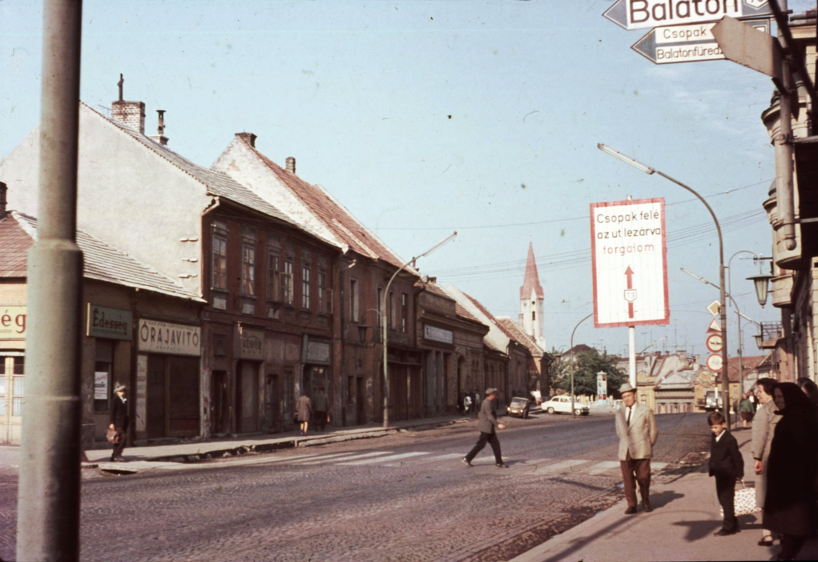 Hungary, Veszprém, Kossuth Lajos utca (mára lebontott) házsora, háttérben az evangélikus templom., 1966, Herth Viktória dr, Bodó Emma, hat, church, colorful, candelabra, street view, lamp post, automobile, clockmaker, board, crosswalk, Fortepan #76518