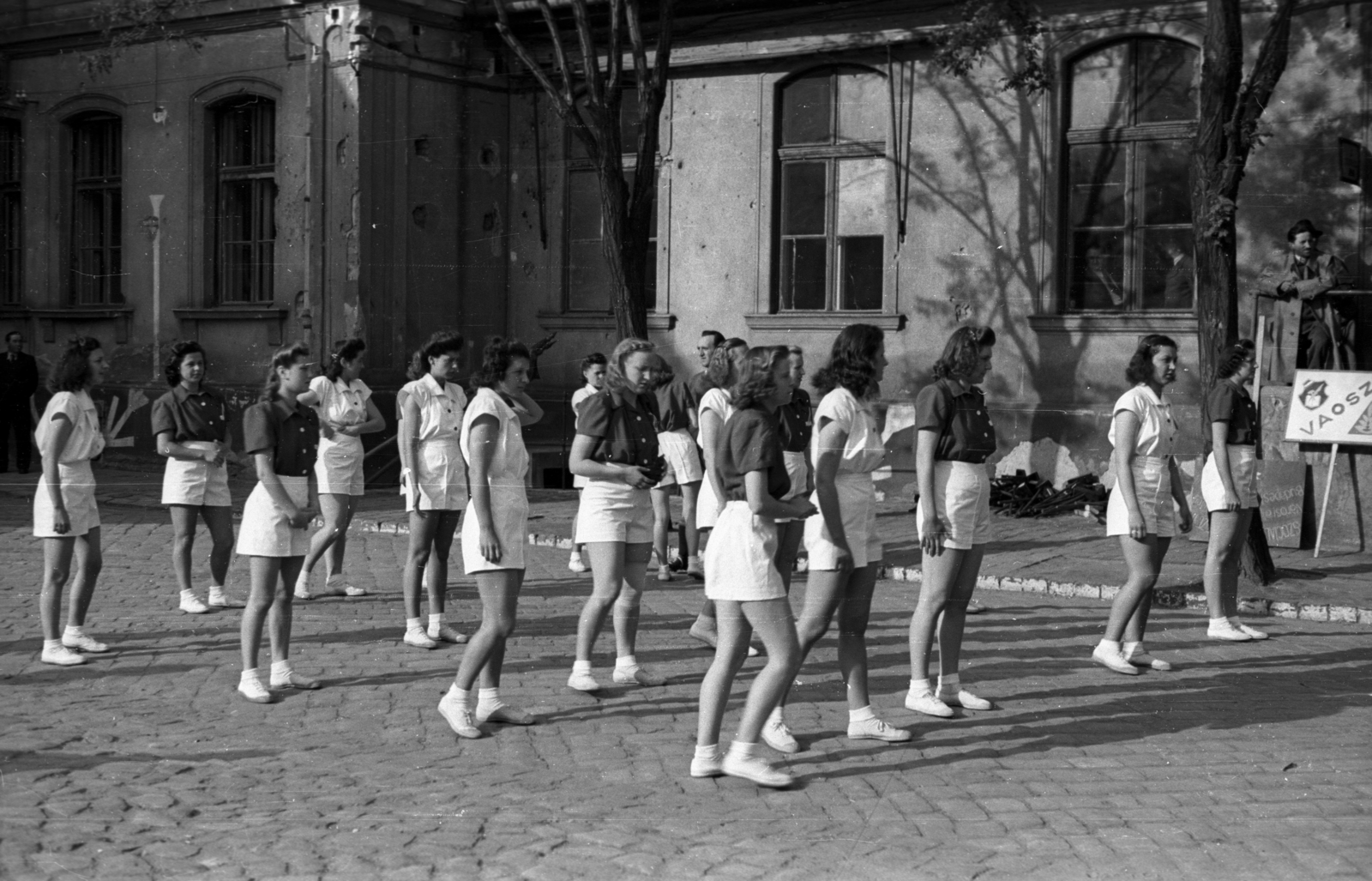 Magyarország, Budapest VIII., II. János Pál pápa (Tisza Kálmán) tér, háttérben a Budapest Székesfőváros Gázmüvei egyik épülete., 1946, Berkó Pál, Budapest, hölgy, fiatalság, golyónyom, egyenruha, sport, Fortepan #79072