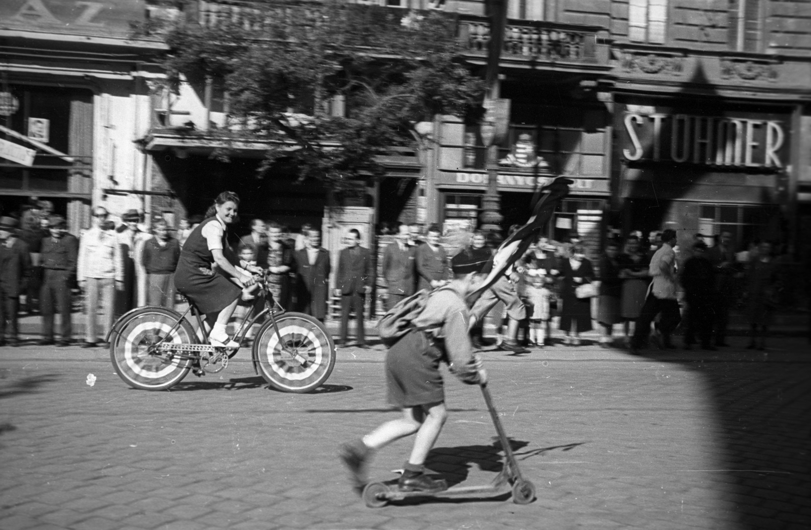 Magyarország, Budapest VII., Erzsébet körút, szemben az EMKE-ház. Május 1-i felvonulás., 1946, Berkó Pál, kerékpár, roller, május 1, trafik, címer, Budapest, cégtábla, sorfal, Stühmer Frigyes csokoládégyár, dísztárcsa, Fortepan #79253