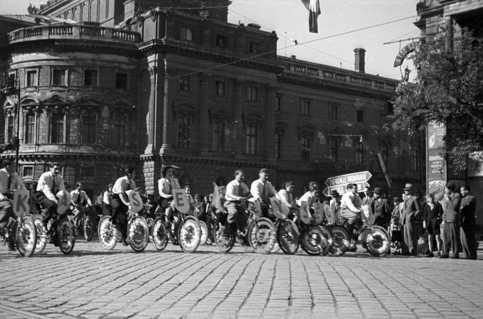 Magyarország, Budapest VIII.,Budapest VII., Erzsébet körút - Rákóczi út kereszteződés, szemben a Blaha Lujza téren a Nemzeti Színház. Május 1-i felvonulás., 1946, Berkó Pál, kerékpár, nemzeti színház, május 1, Fellner és Helmer-terv, eklektikus építészet, Budapest, dísztárcsa, Fortepan #79254