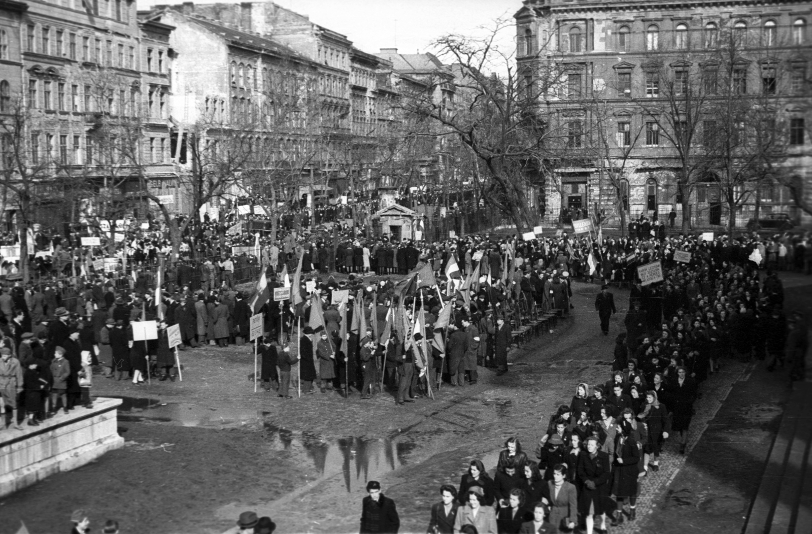 Magyarország, Budapest VIII., Múzeumkert, március 15-i ünnepség. Háttérben a Múzeum körút - Bródy Sándor utca találkozása., 1947, Berkó Pál, Budapest, felvonulás, pocsolya, tábla, zászló, Fortepan #79373