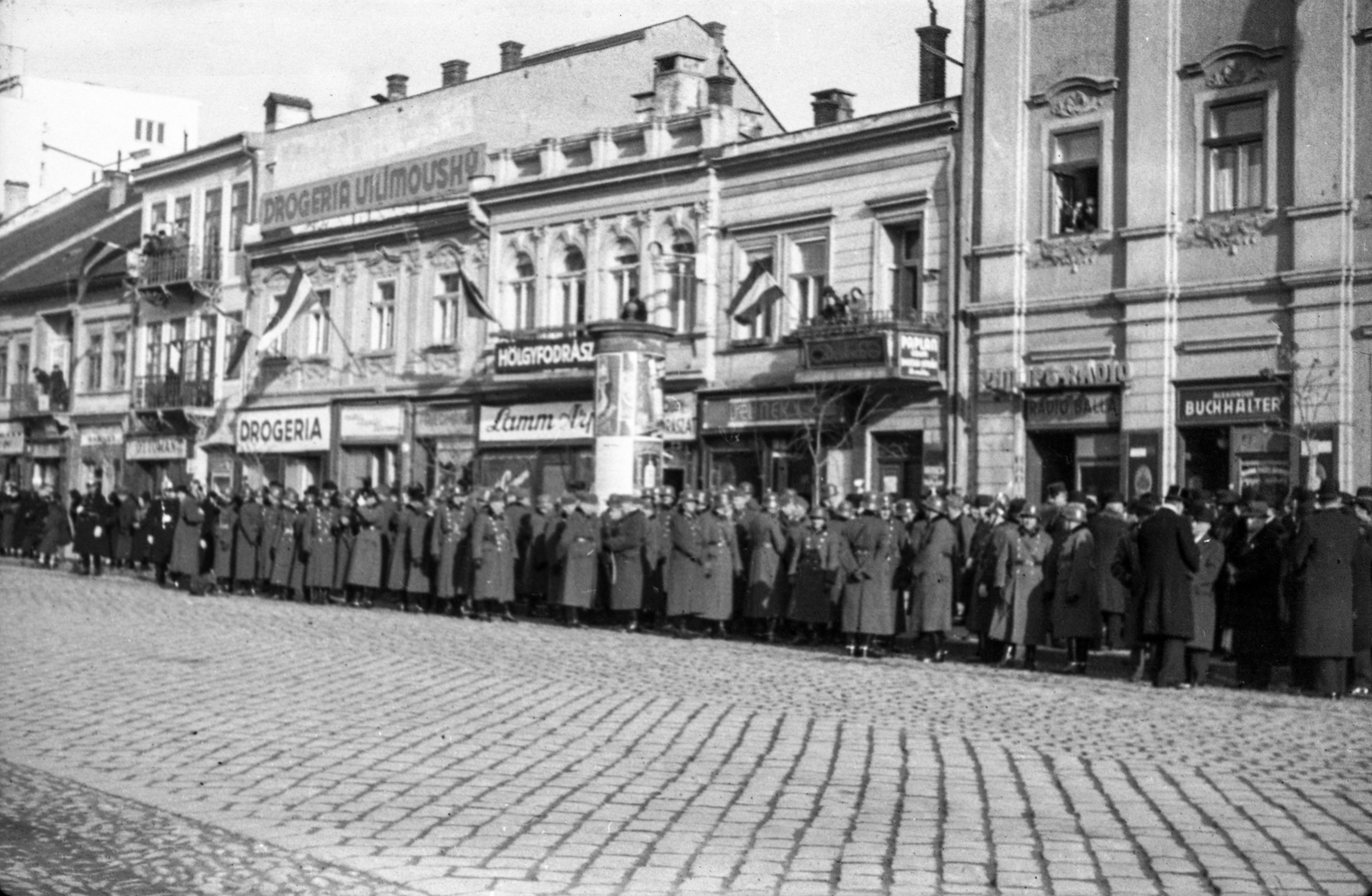 Szlovákia, Kassa, Fő utca (ulica Hlavná)., 1939, Berkó Pál, zászló, cégtábla, tömeg, hirdetőoszlop, fodrászat, katona, kockakő, drogéria, Fortepan #79523