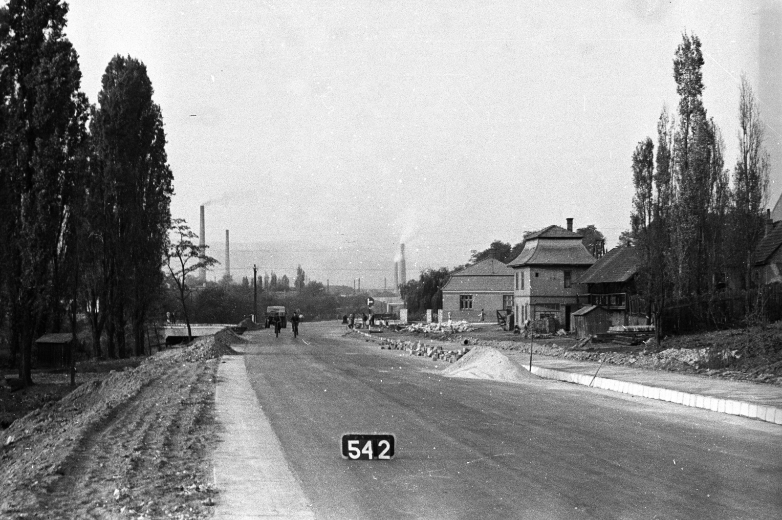 Hungary, Tata-Tóváros, 1-es főút a felsőgallai Szabadság térnél, szemben a Budapest-Hegyeshalom vasútvonal (később iparvágányok) felüljárója, háttérben a Cement- és Mészmű kéményei., 1961, UVATERV, bicycle, commercial vehicle, chimney, road construction, fir, Fortepan #80159